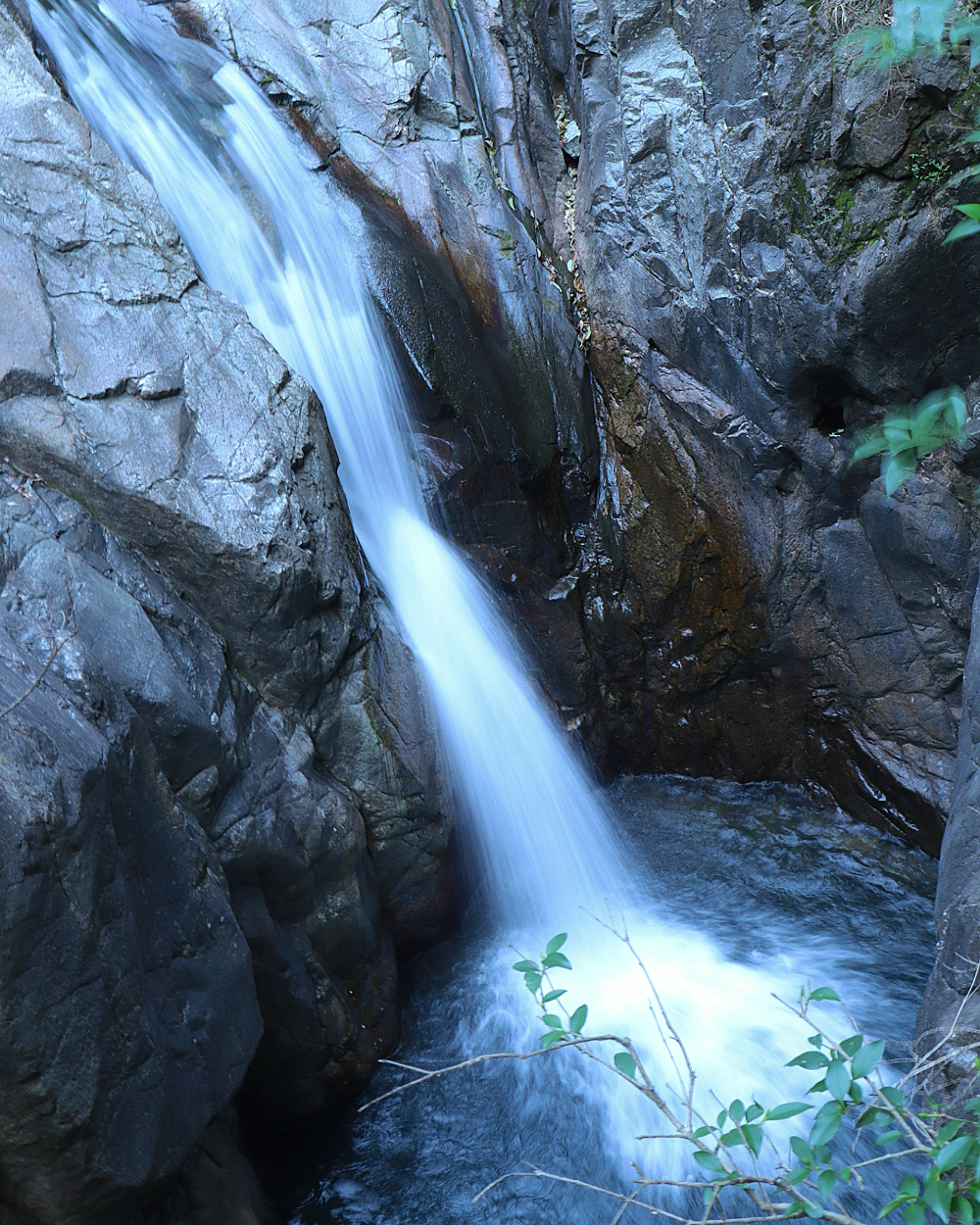 Sebuah air terjun mengalir di antara tebing berbatu ke kolam yang tenang