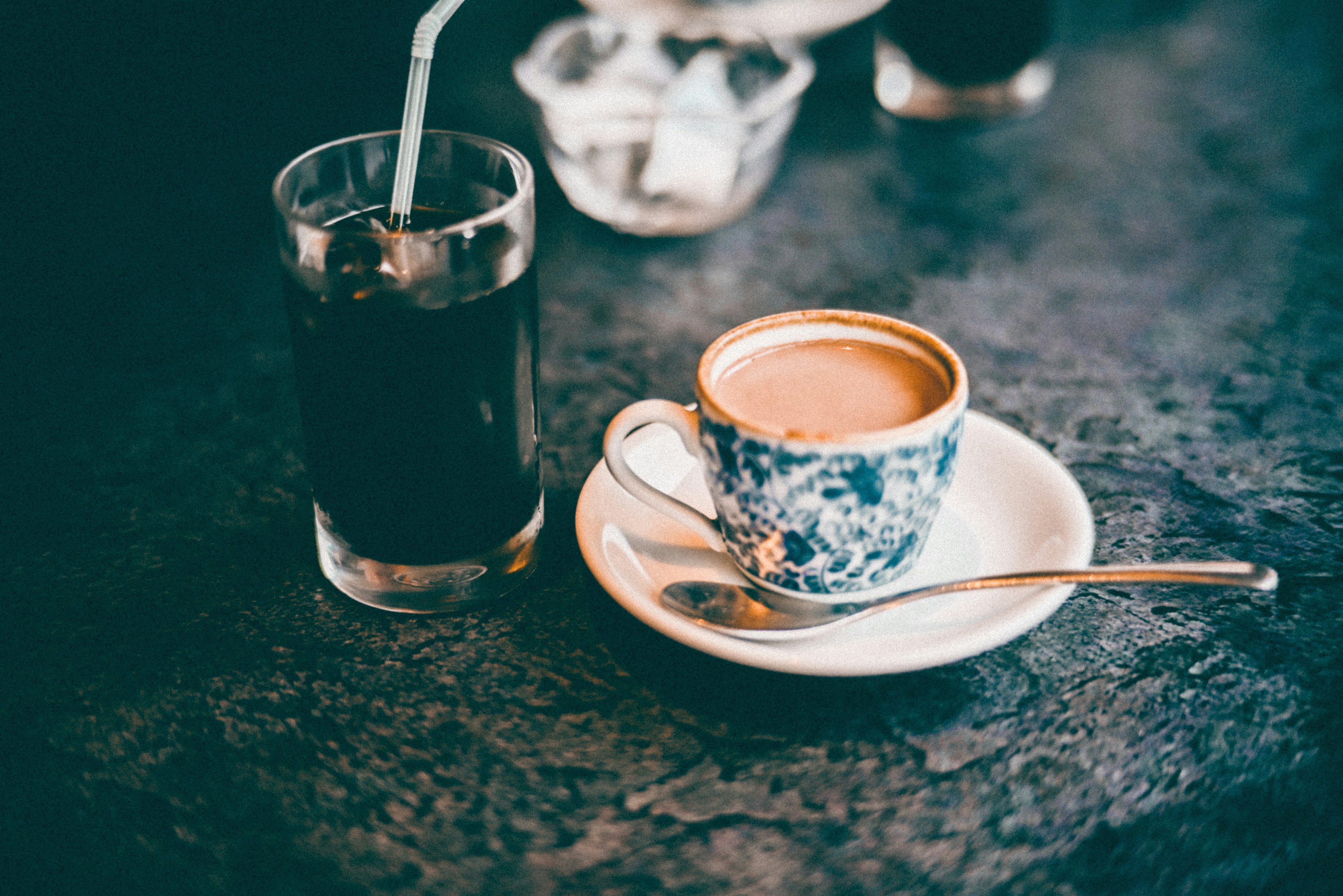 A coffee cup and a glass of iced drink on a cafe table