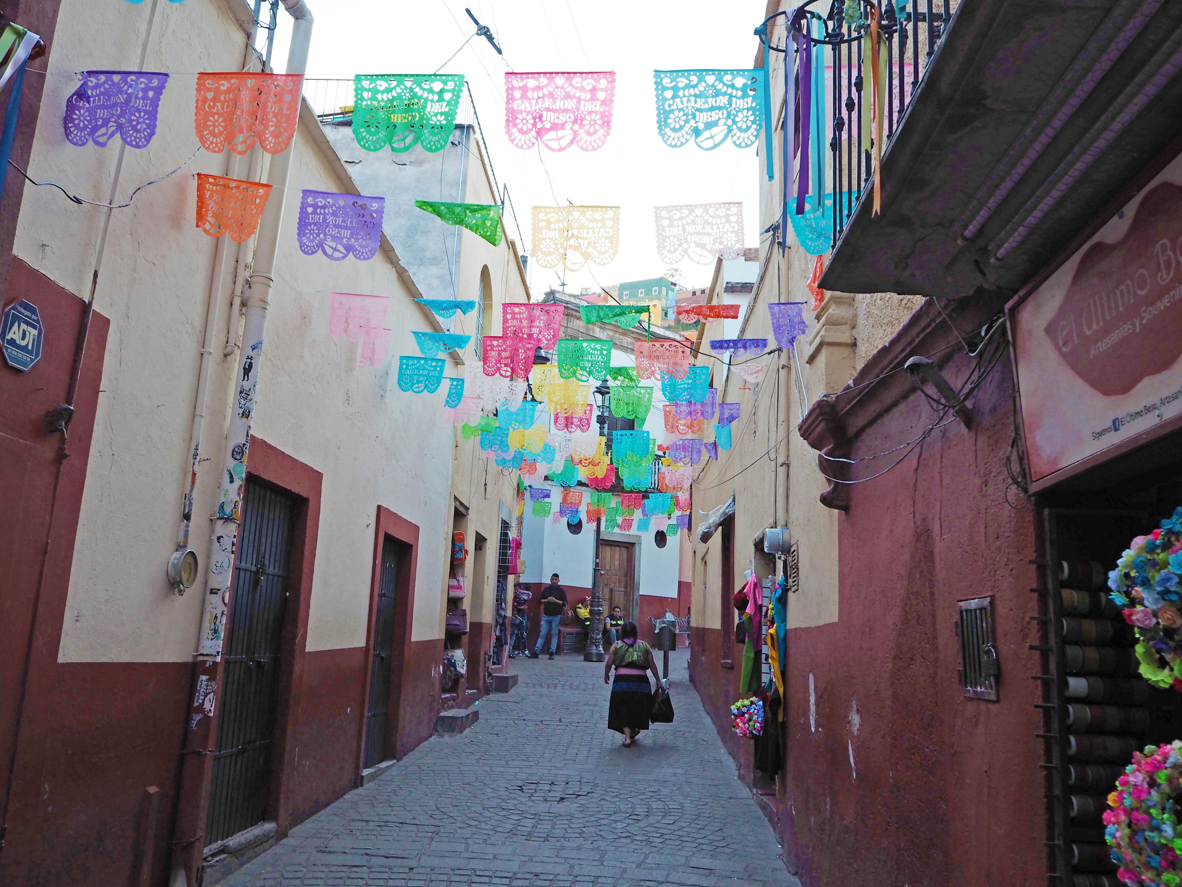 一位女性走在装饰有 papel picado 的多彩墨西哥小巷中