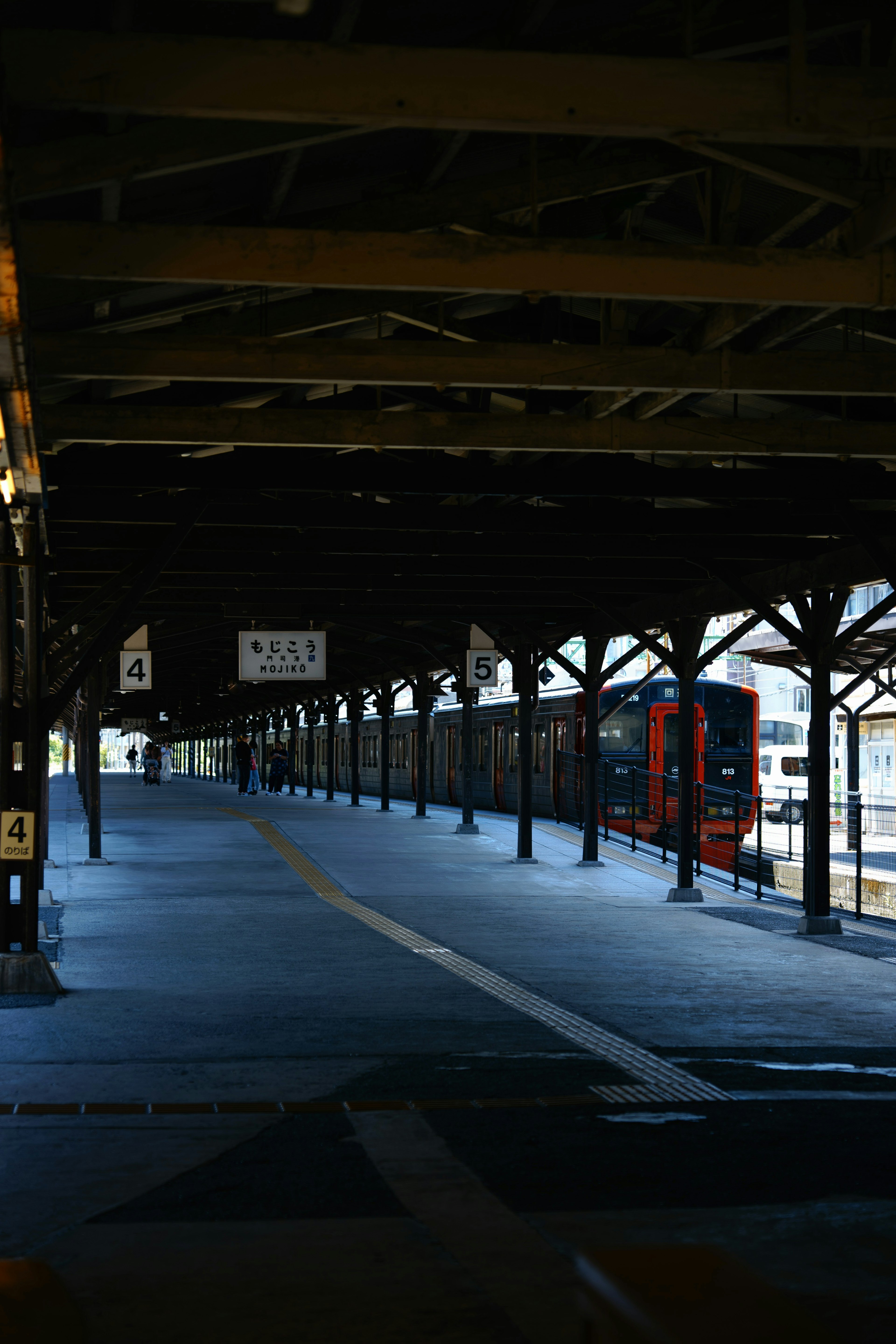 古い駅のプラットフォームで、木製の梁と赤い列車が見える