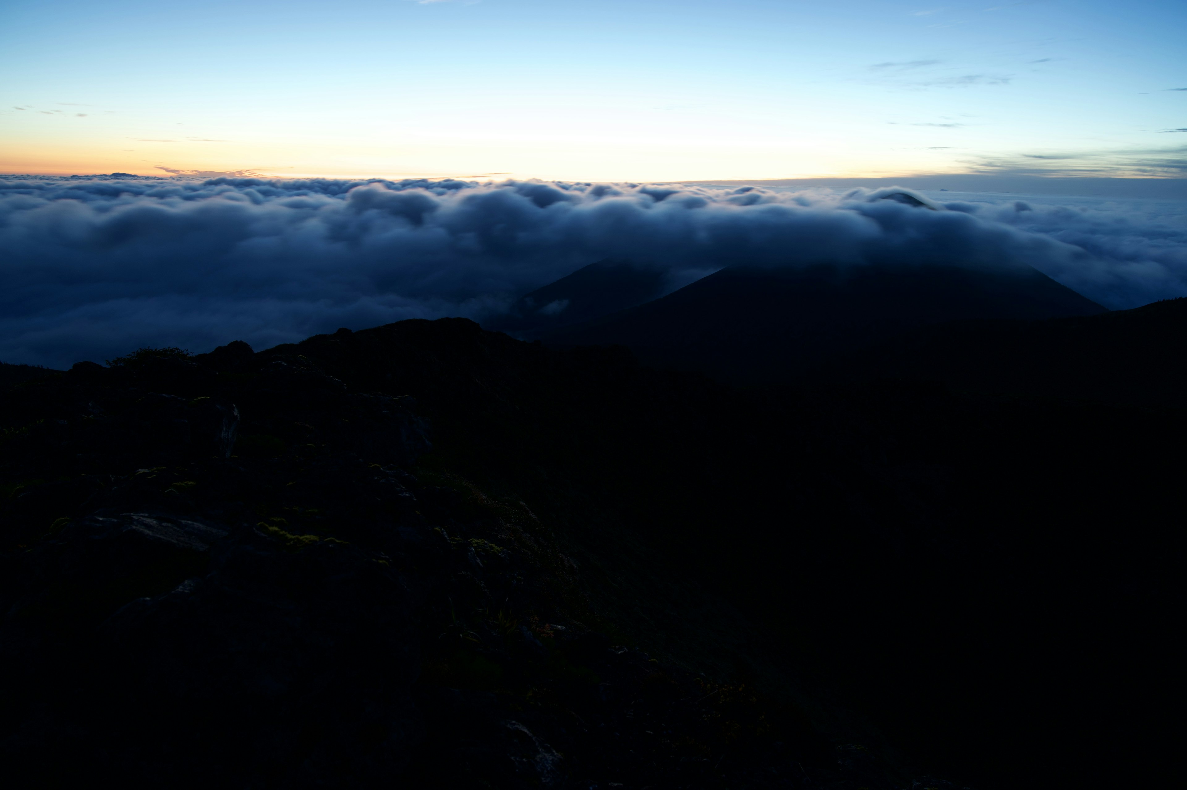 Vista da un picco di montagna all'alba con un mare di nuvole e un cielo blu