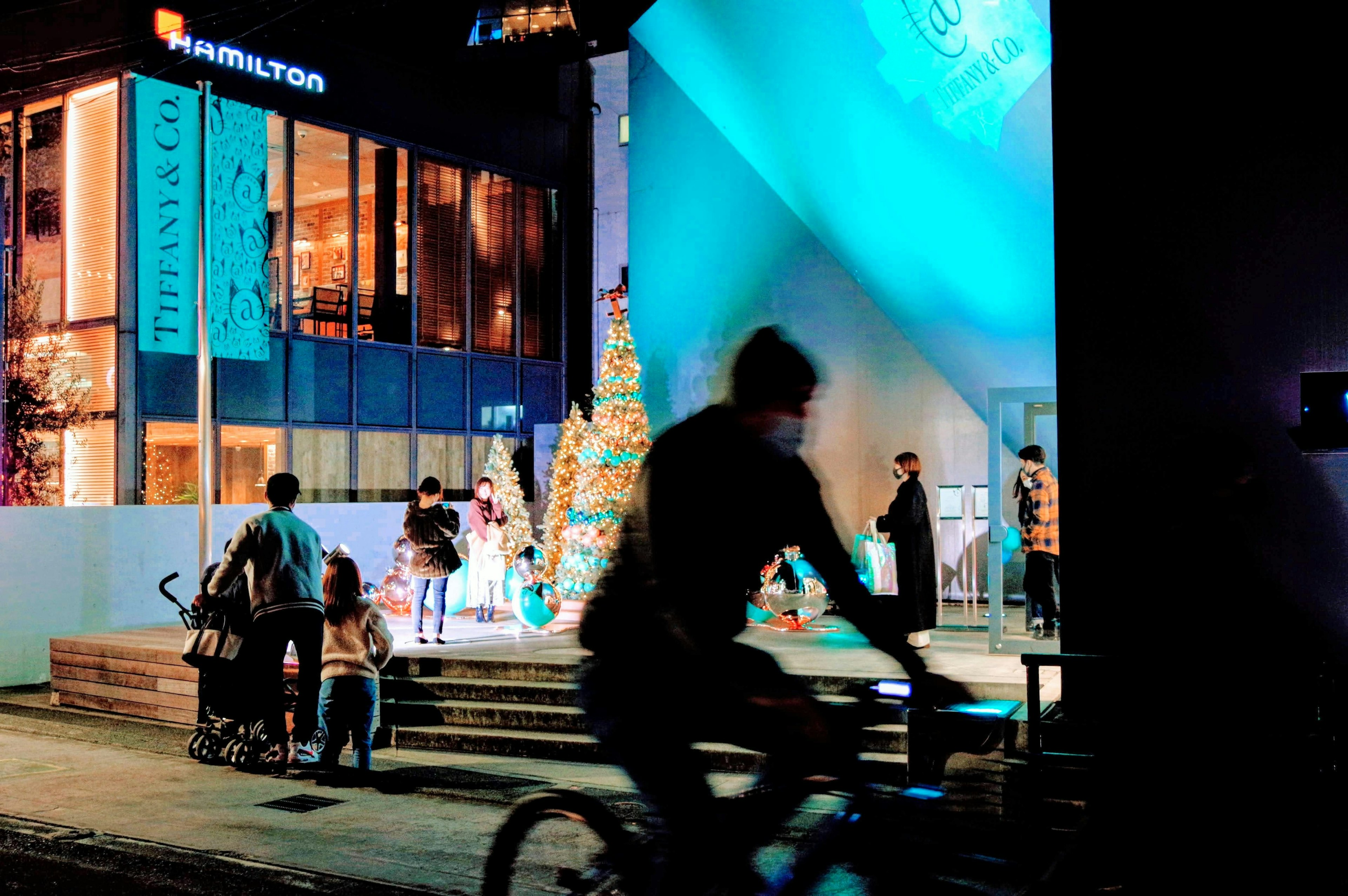 人が自転車に乗っている夜の街の風景 ハミルトンの看板と青い照明がある背景