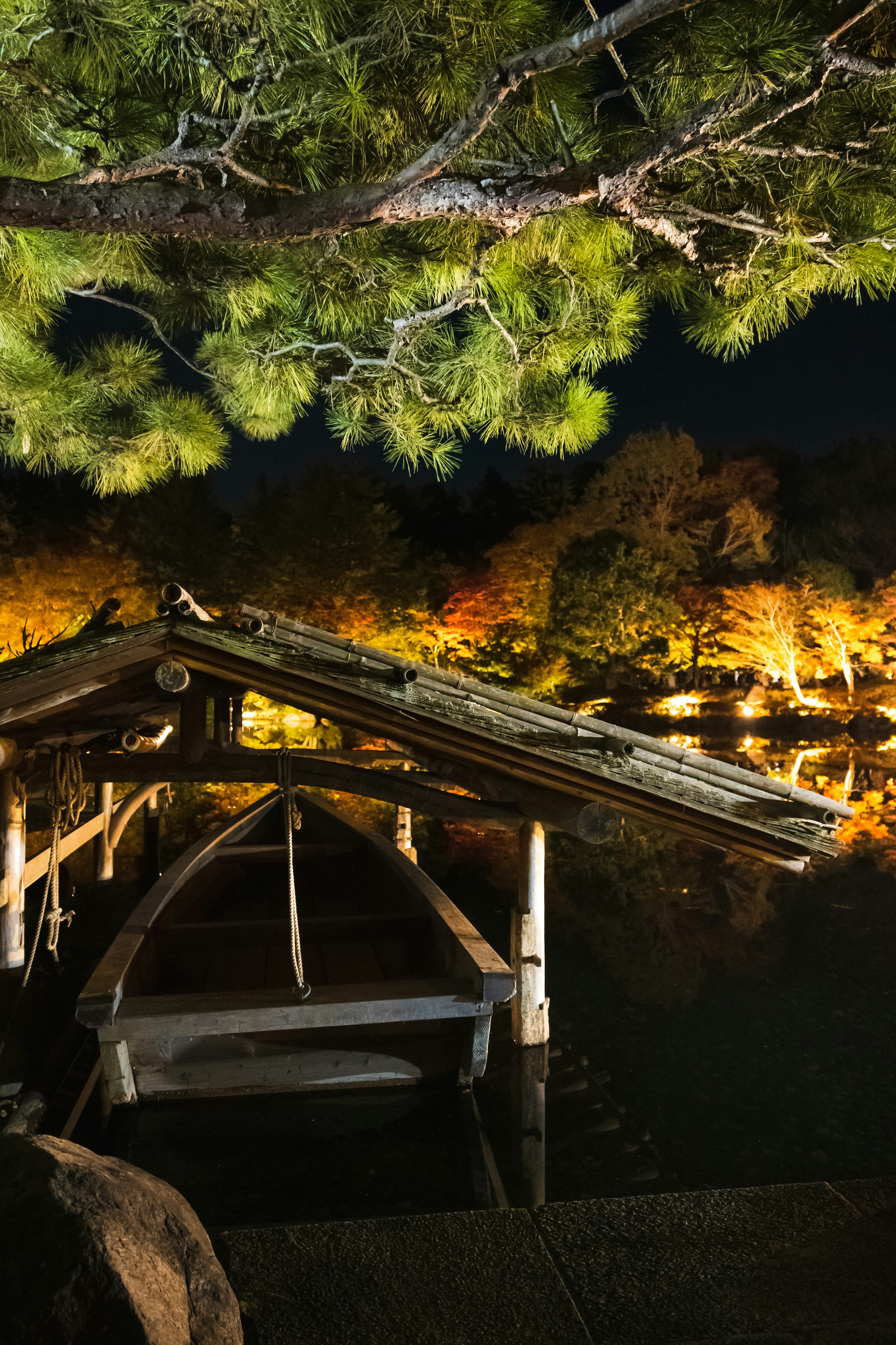 A serene lakeside view featuring a wooden boat and a shelter at night with vibrant reflections