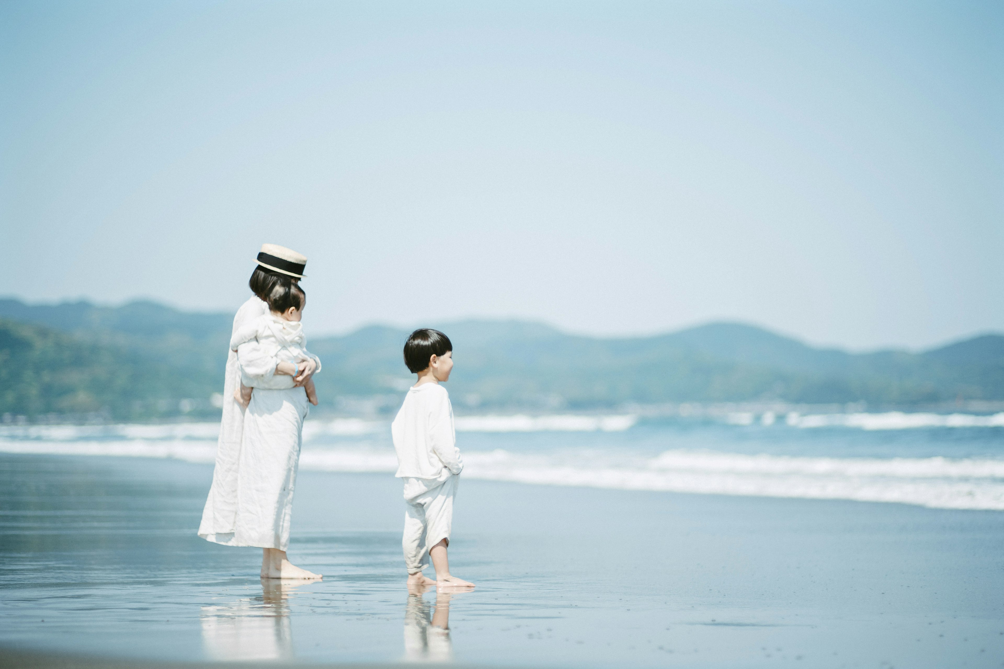 A woman in white standing with a child at the beach