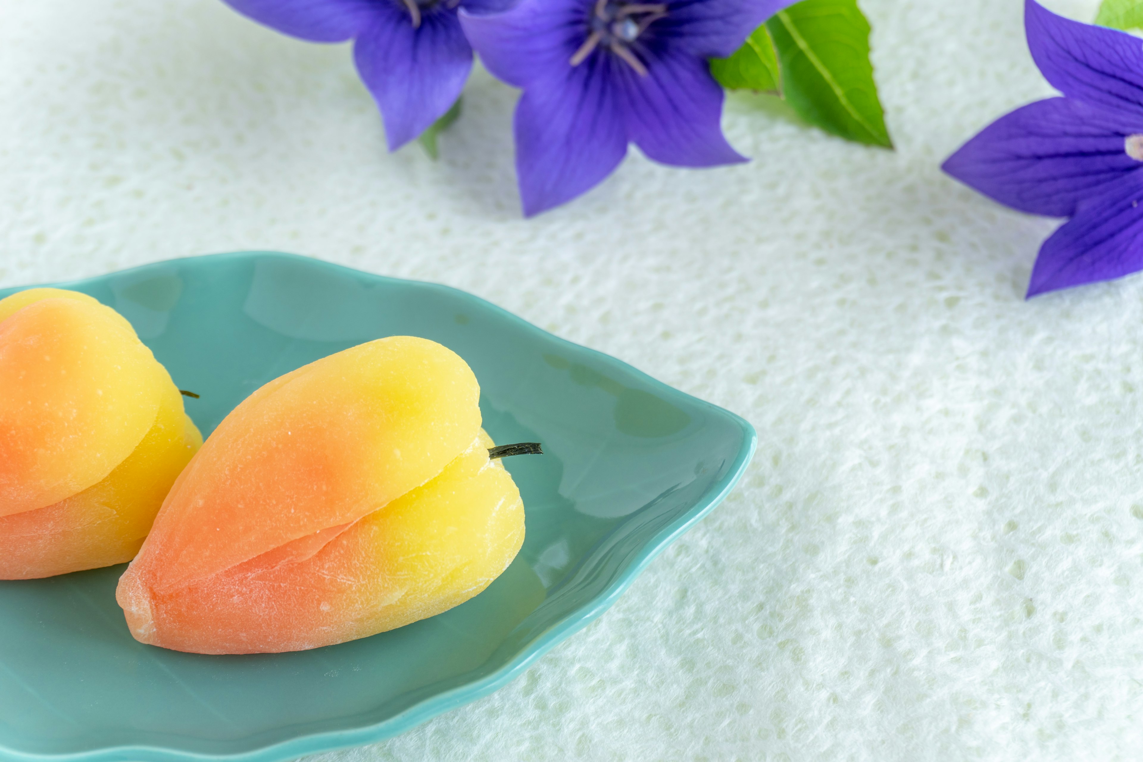 Desserts en forme de pêche sur une assiette bleue avec des fleurs violettes en arrière-plan