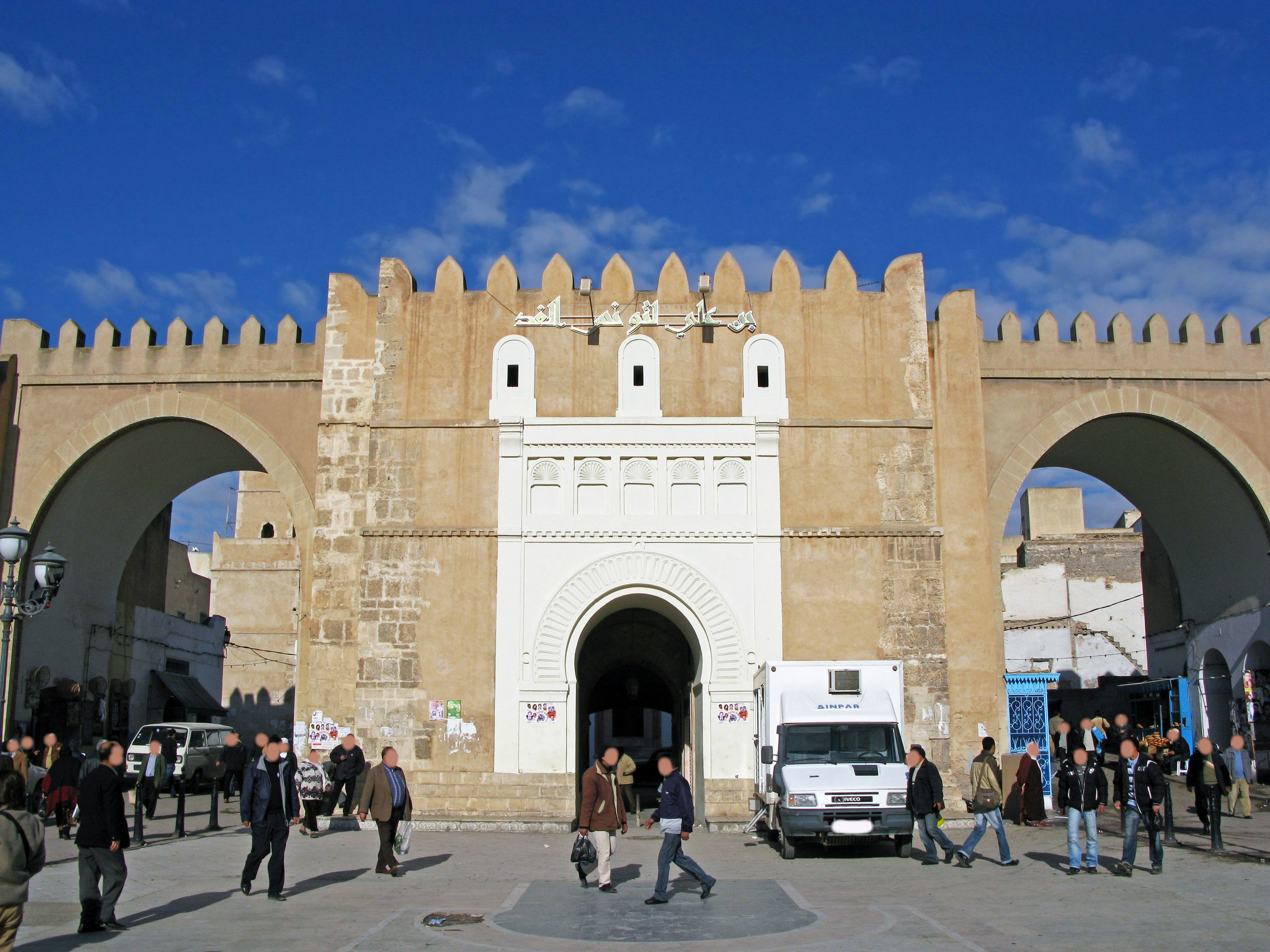 Porte historique avec des personnes marchant sous un ciel bleu