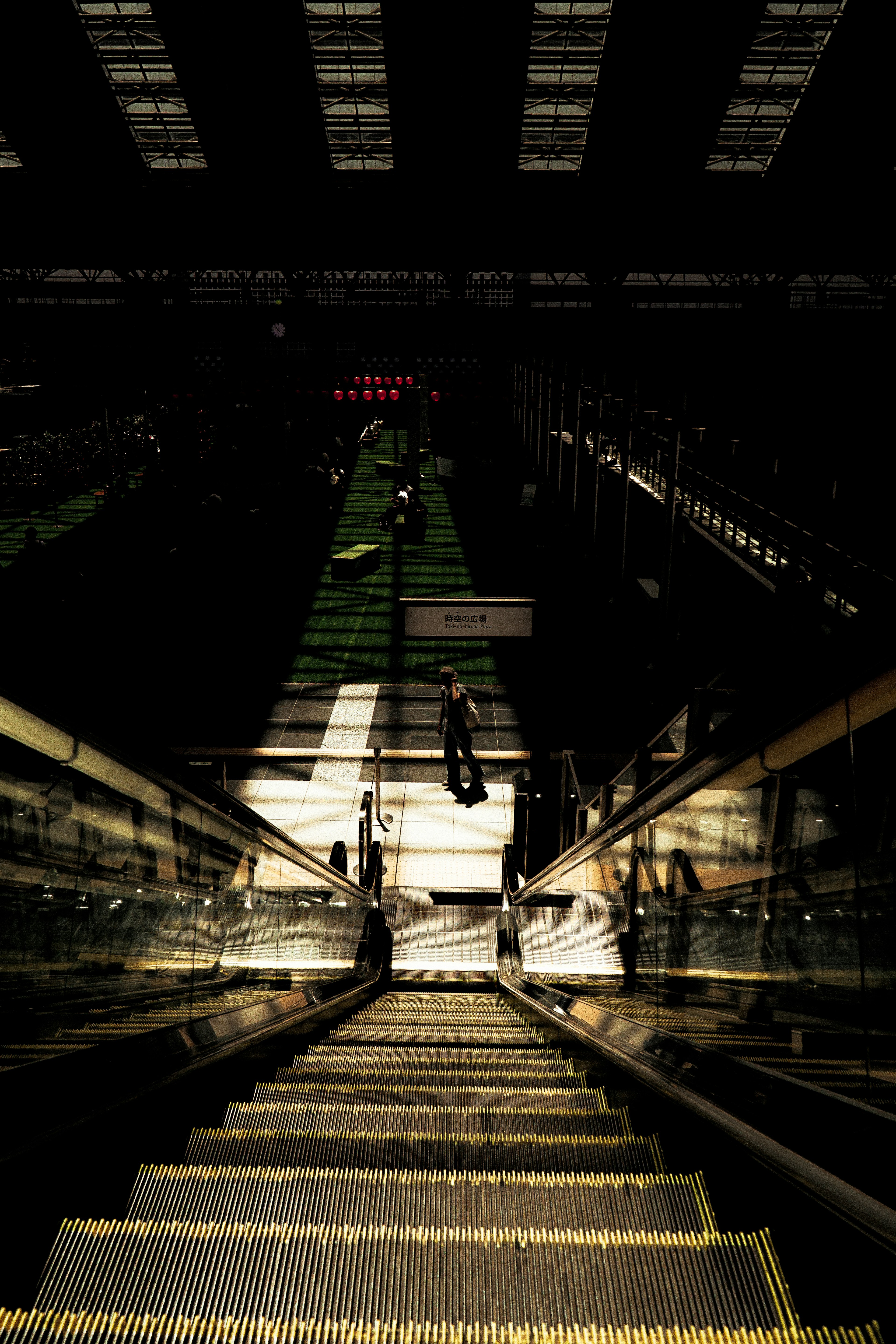 View down an escalator in a shopping mall featuring contrasting light and shadows