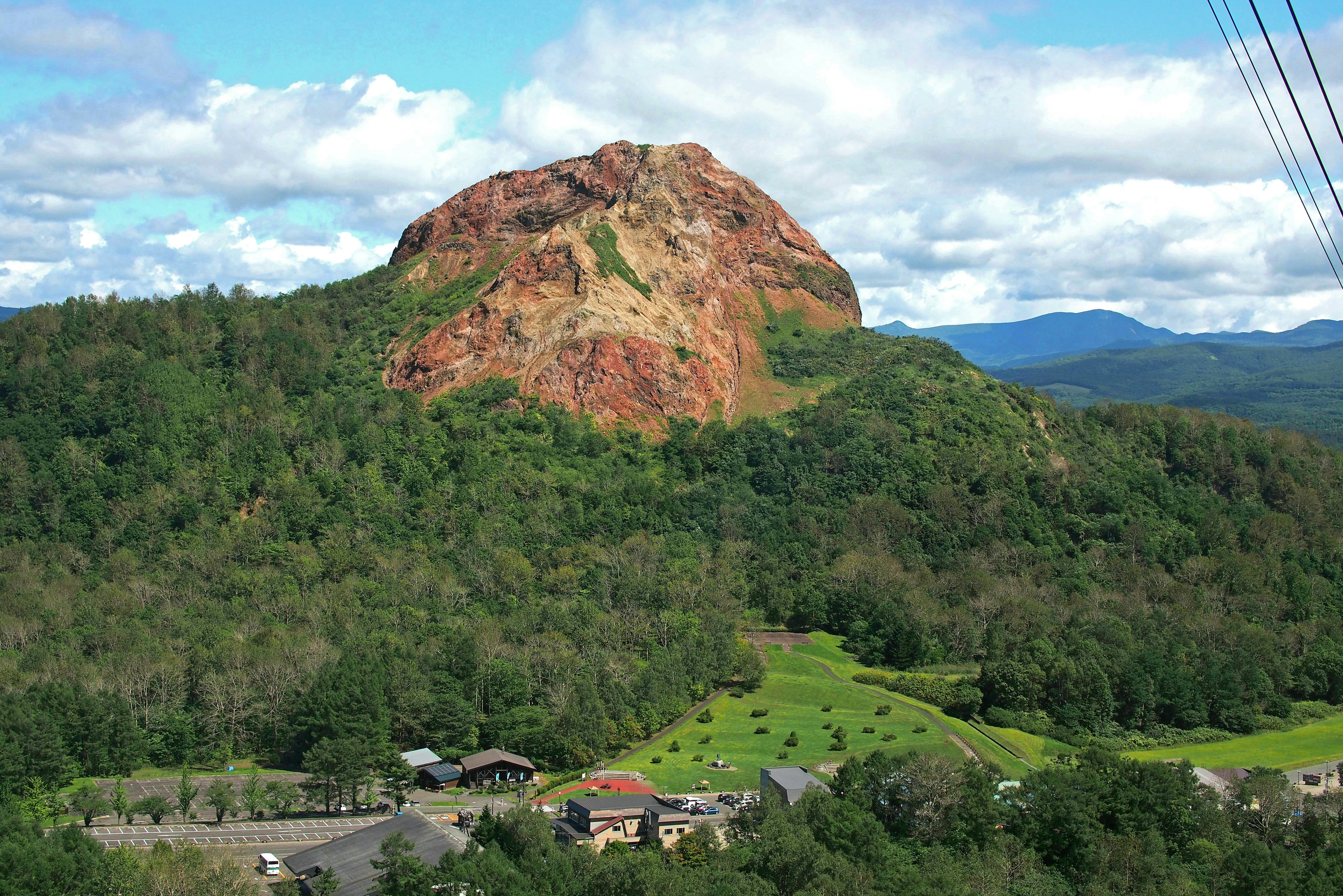 Pemandangan bukit merah dikelilingi hutan hijau