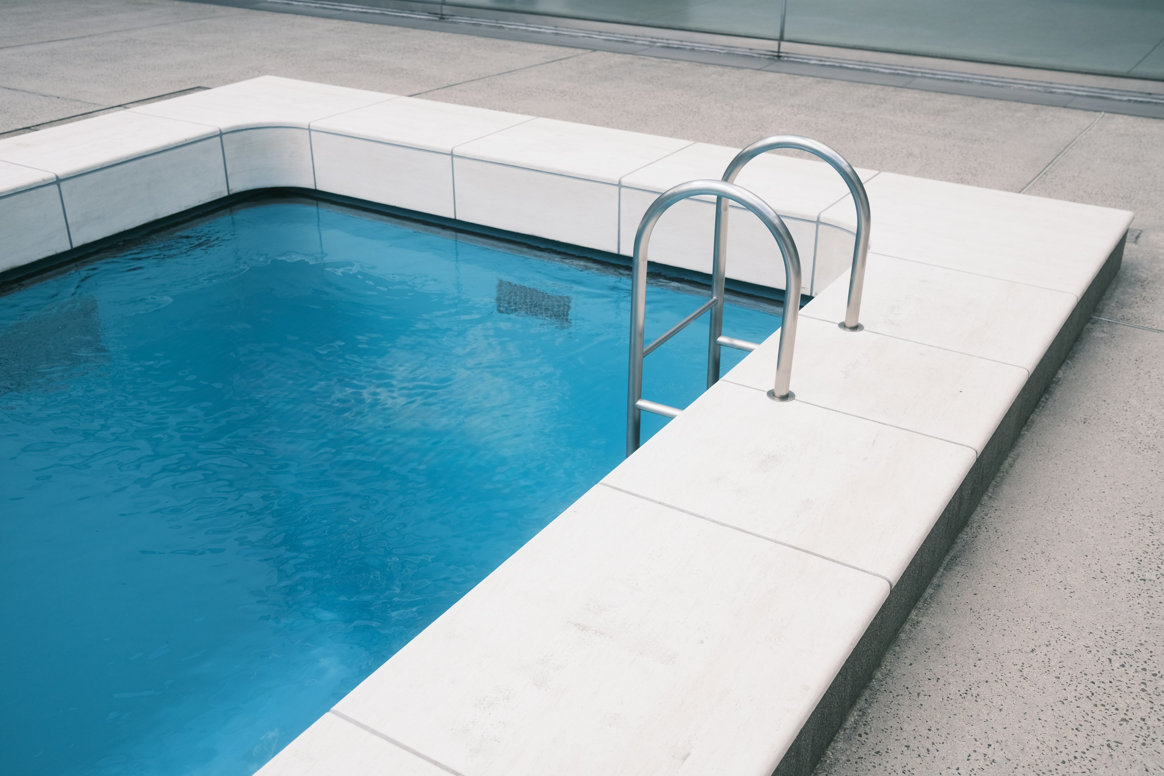 Piscine bleue avec échelle en métal et bords en carreaux blancs