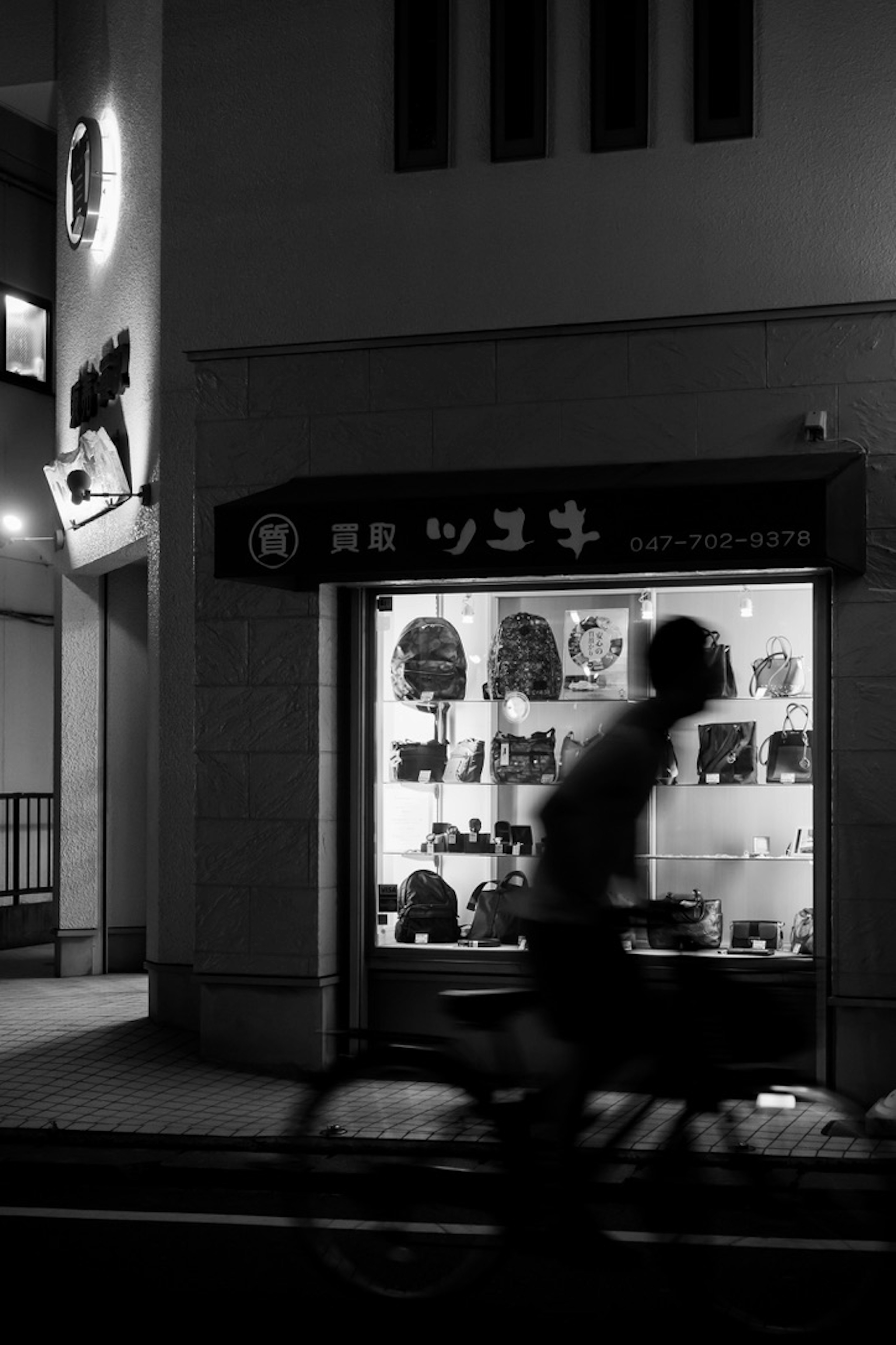 Silueta de una persona montando en bicicleta frente a una ventana de tienda por la noche