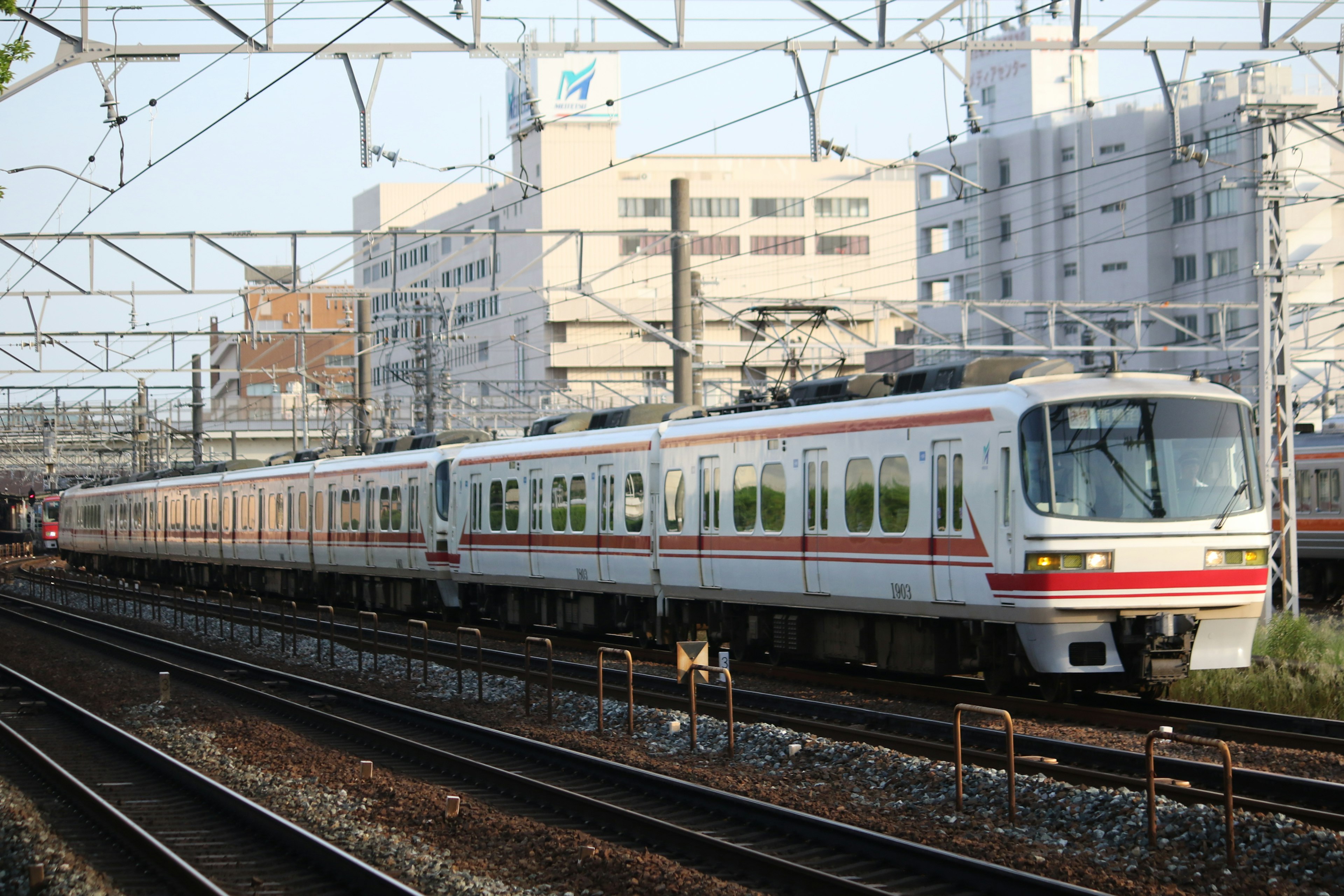 รถไฟสีขาวและแดงวิ่งบนรางพร้อมอาคารอยู่เบื้องหลัง