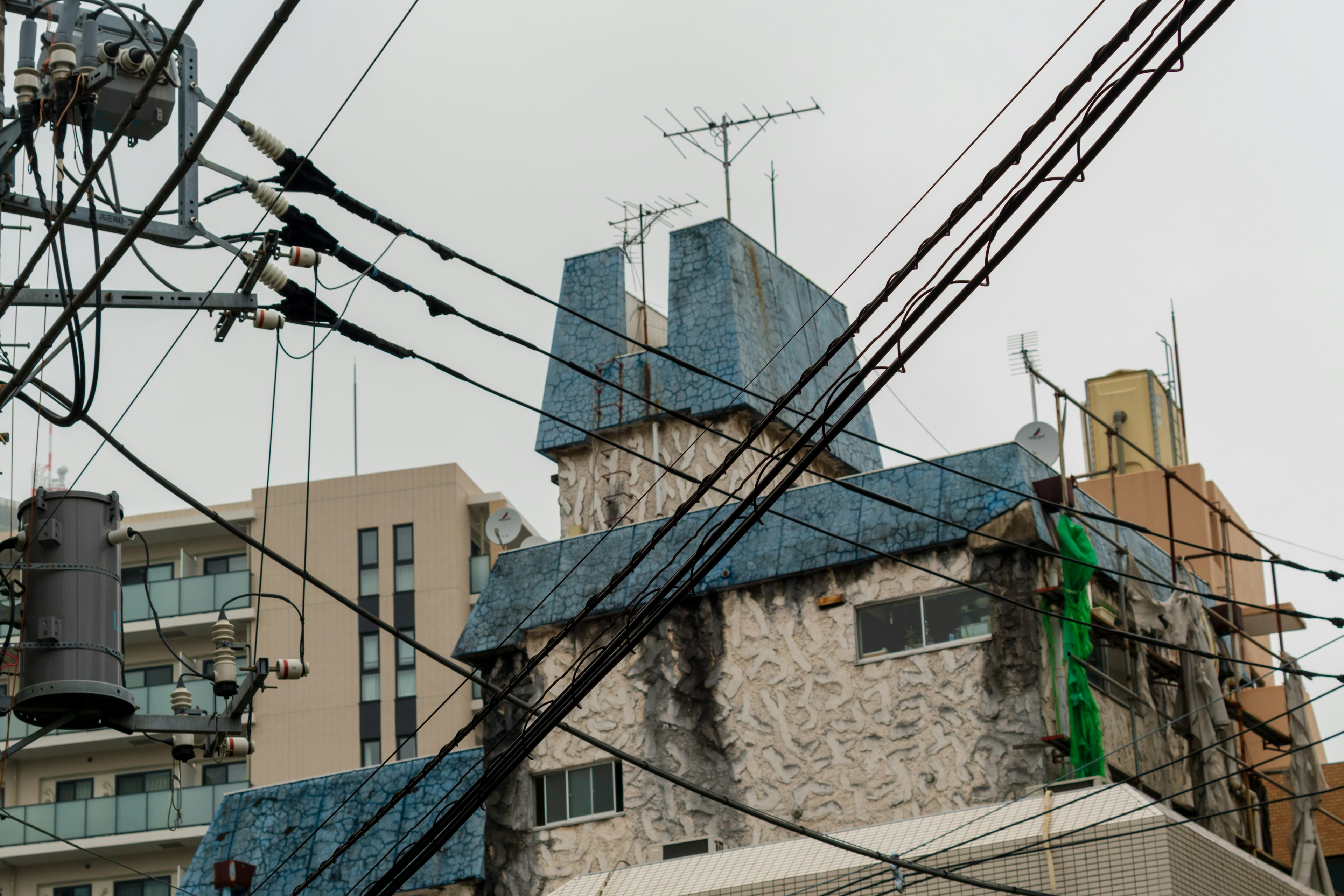 Edificio único con techo azul y líneas eléctricas cruzadas en un paisaje urbano