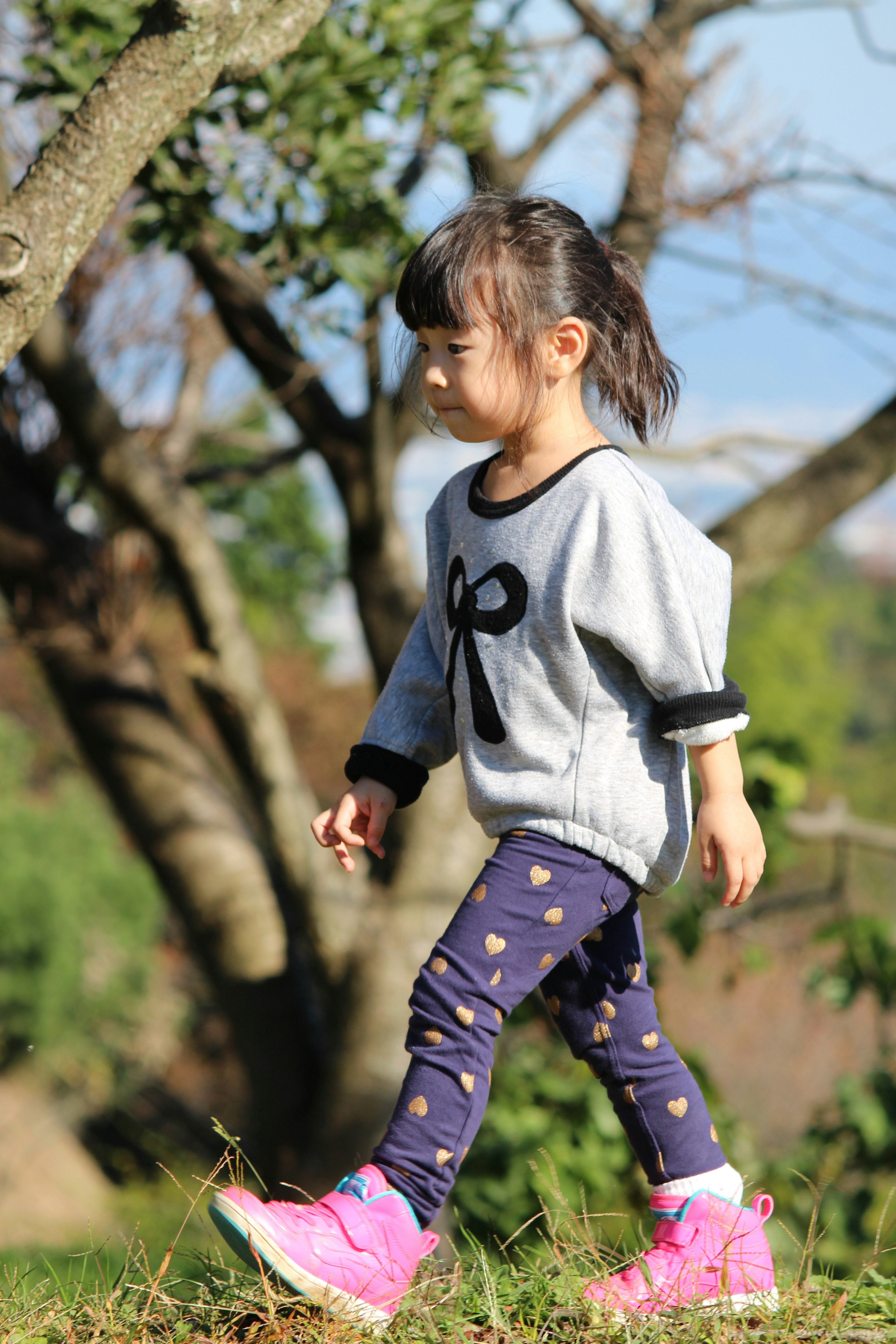 Una niña caminando en un parque con un suéter gris y pantalones con estampado de estrellas y zapatos rosas