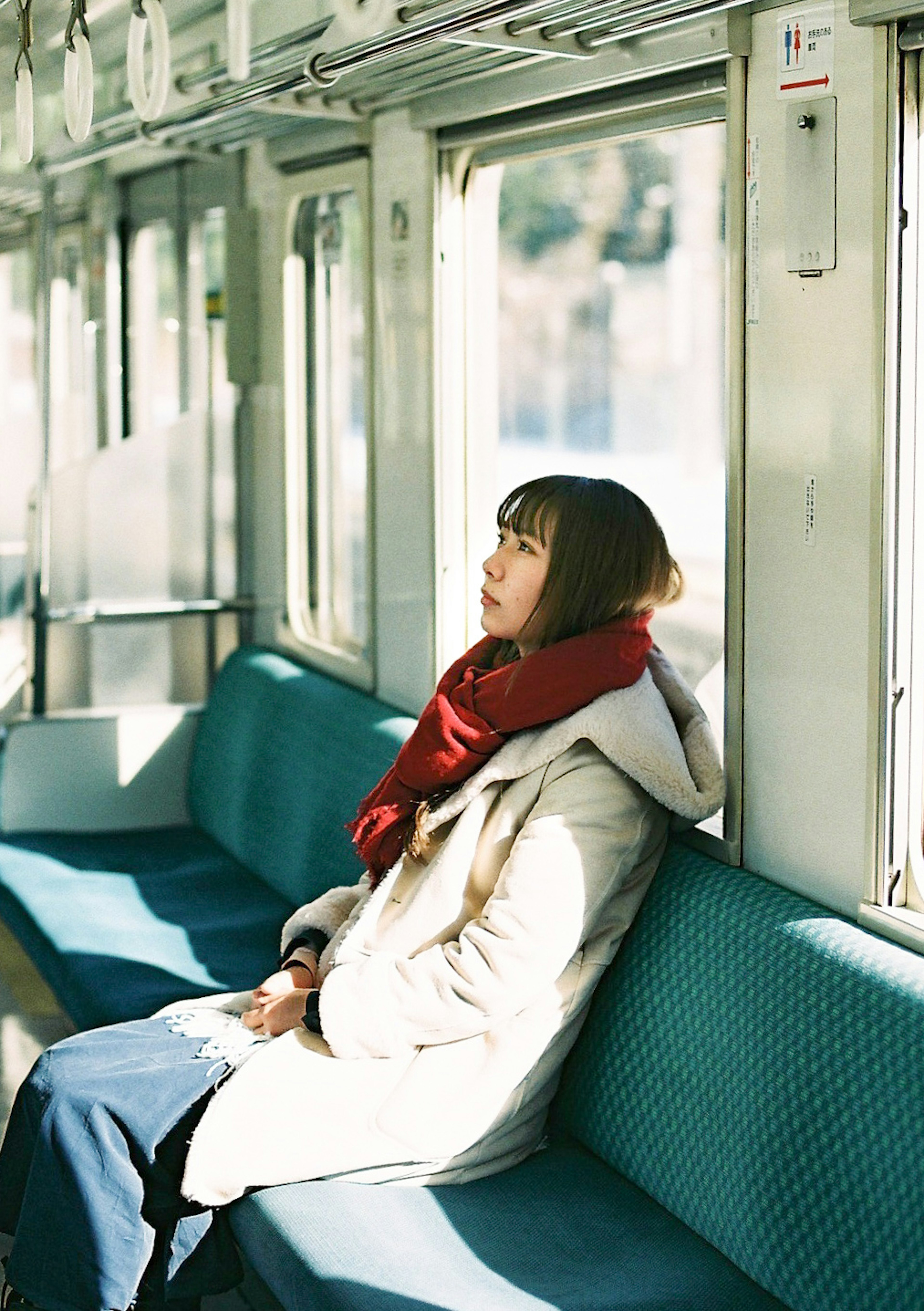 A woman sitting quietly inside a train wearing a red scarf by the window