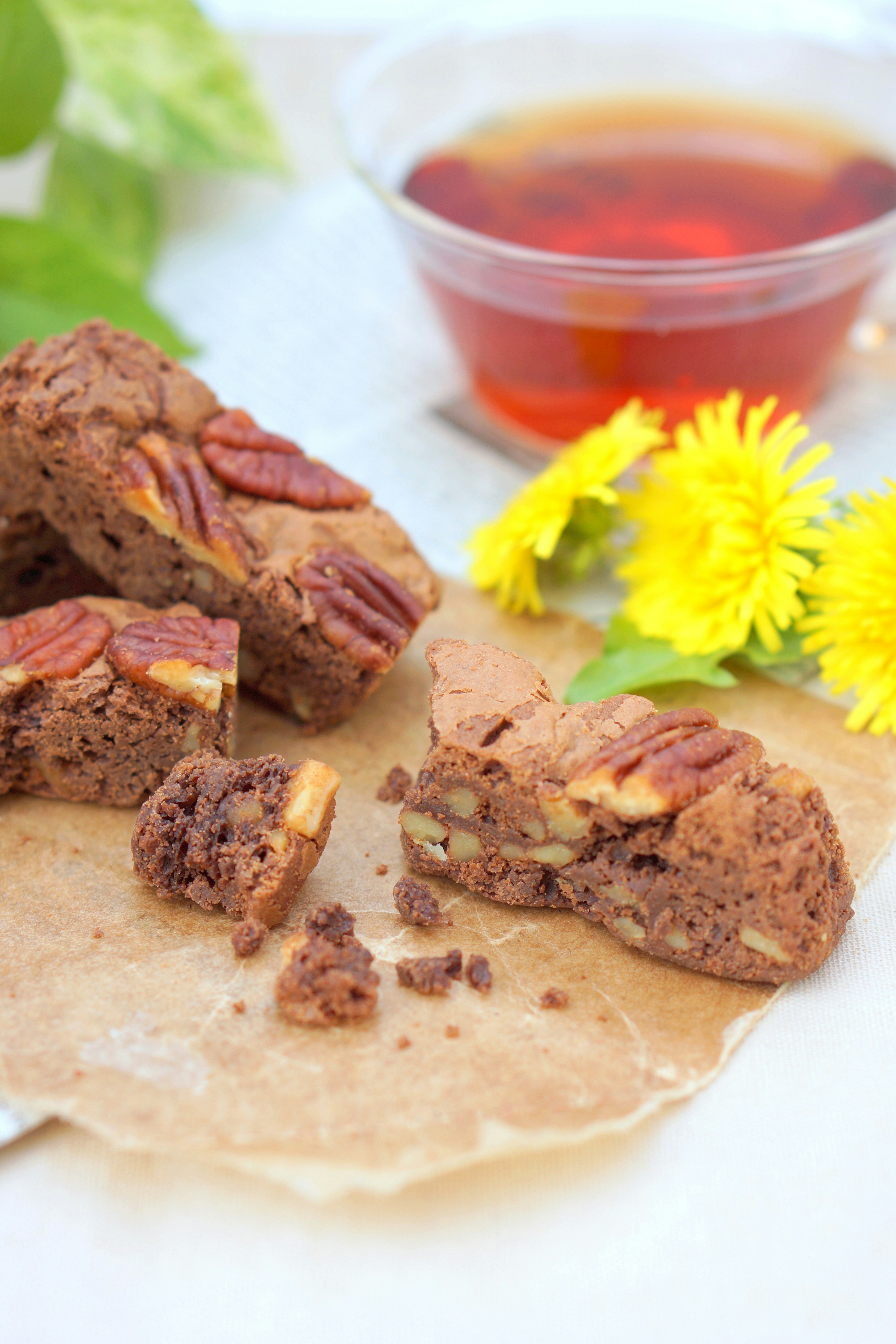 Un conjunto de brownies de nuez acompañado de té de hierbas con flores amarillas cerca