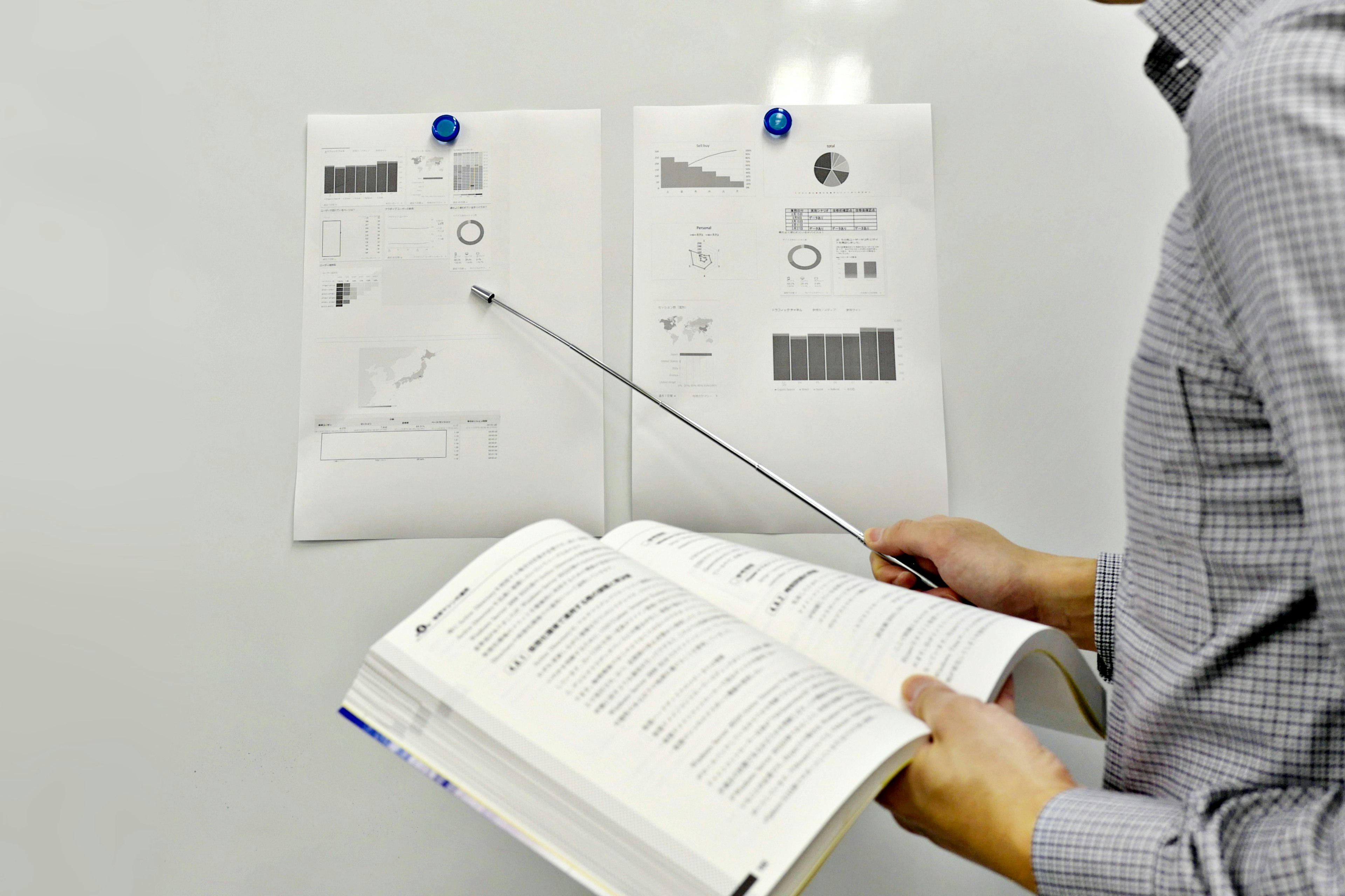 A man holding a textbook and pointing at documents on a whiteboard with a pointer