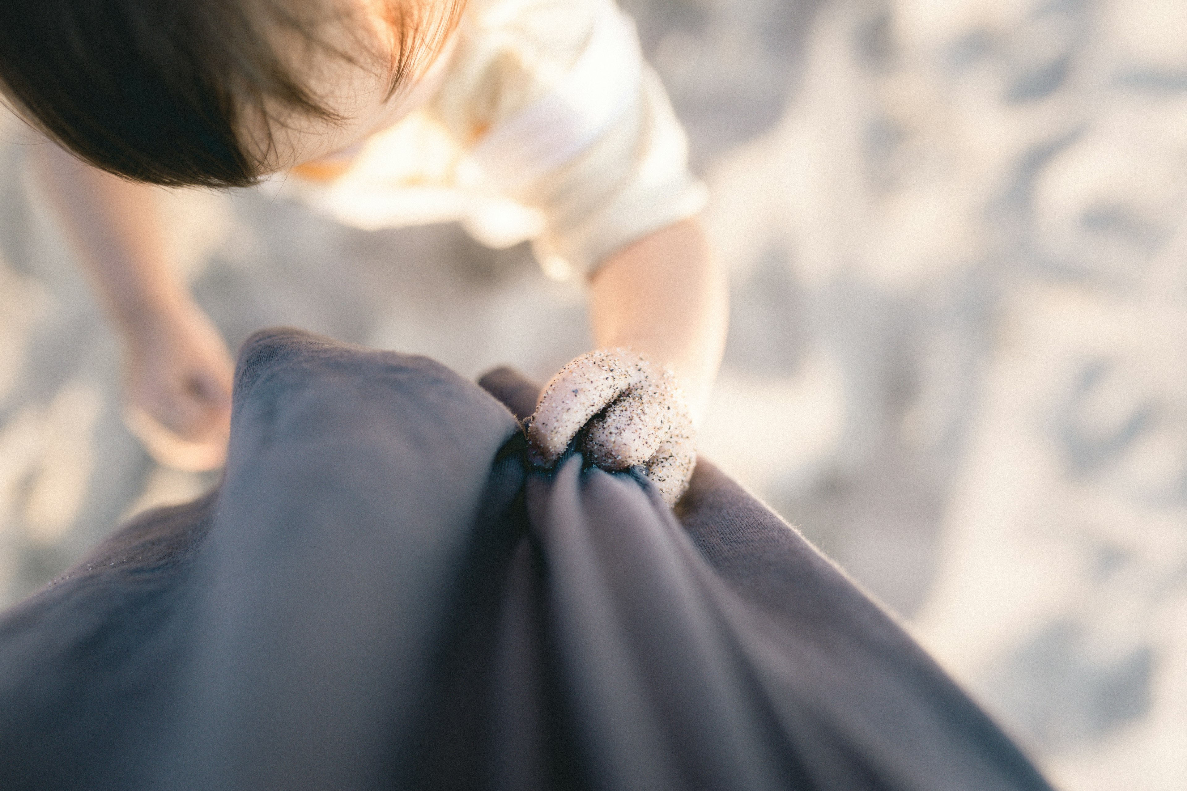 A child grasping fabric from an overhead perspective with soft beach colors