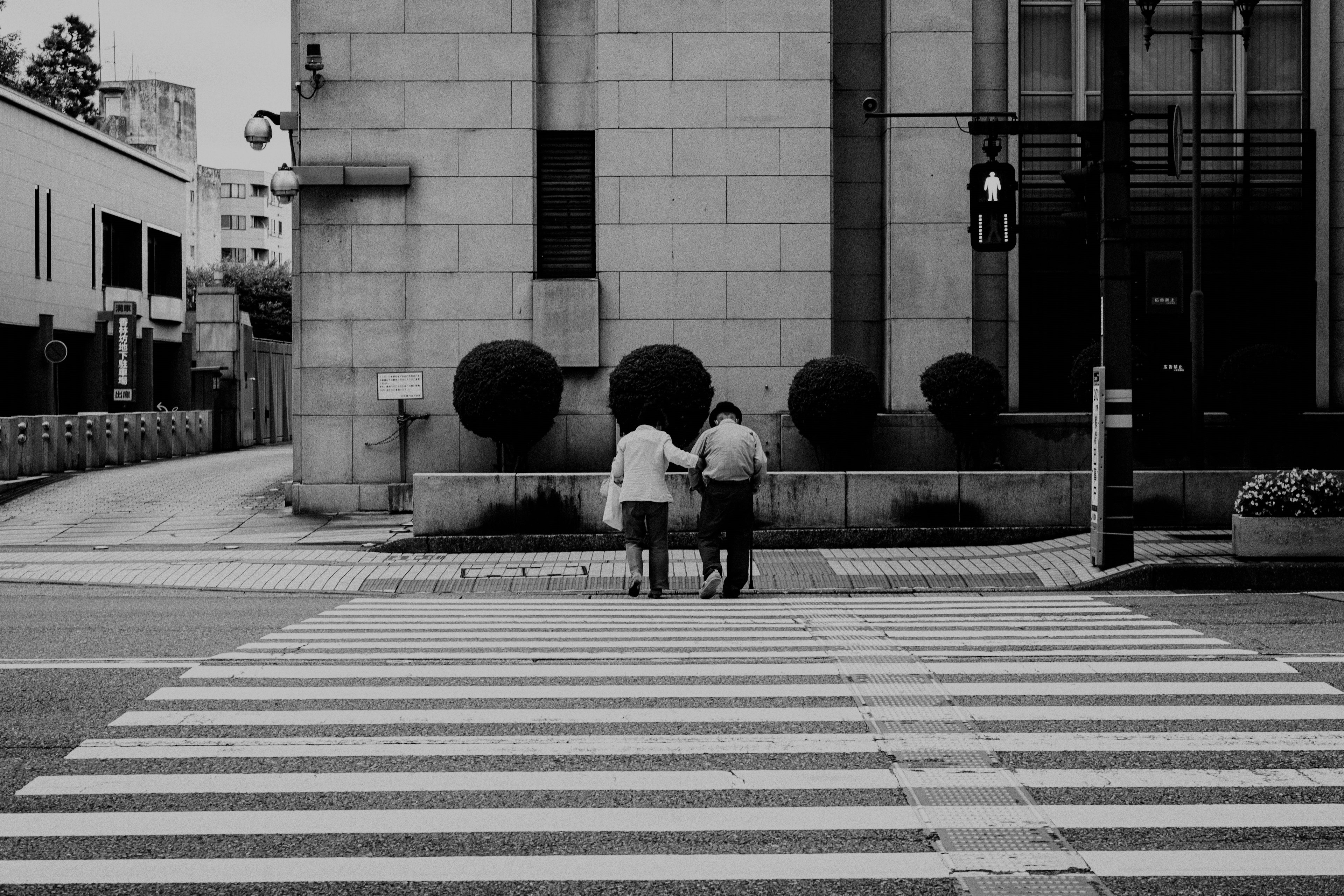 Foto in bianco e nero di due anziani che si tengono per mano mentre attraversano un attraversamento pedonale