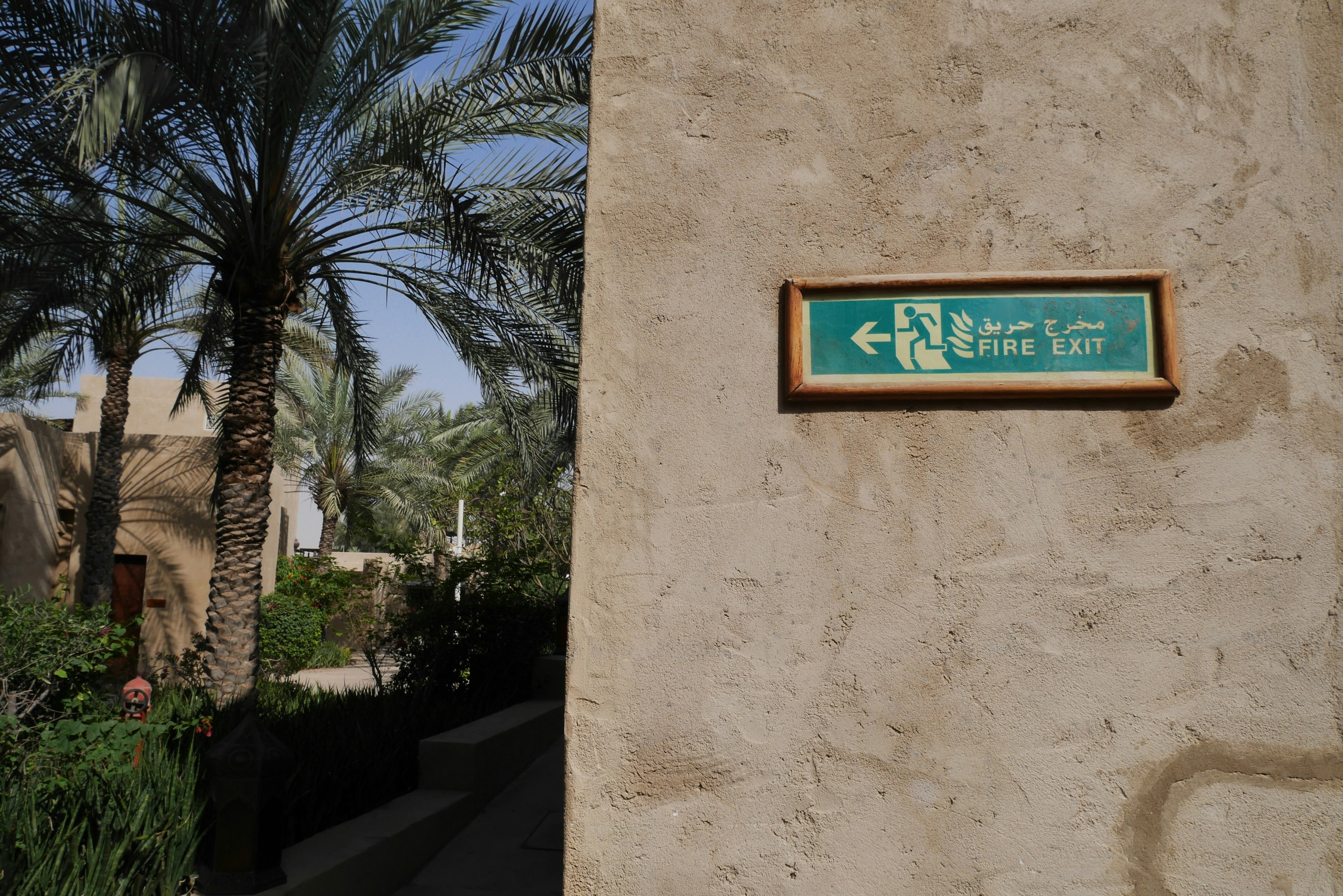 A green sign mounted on a wall indicating left direction with palm trees in the background