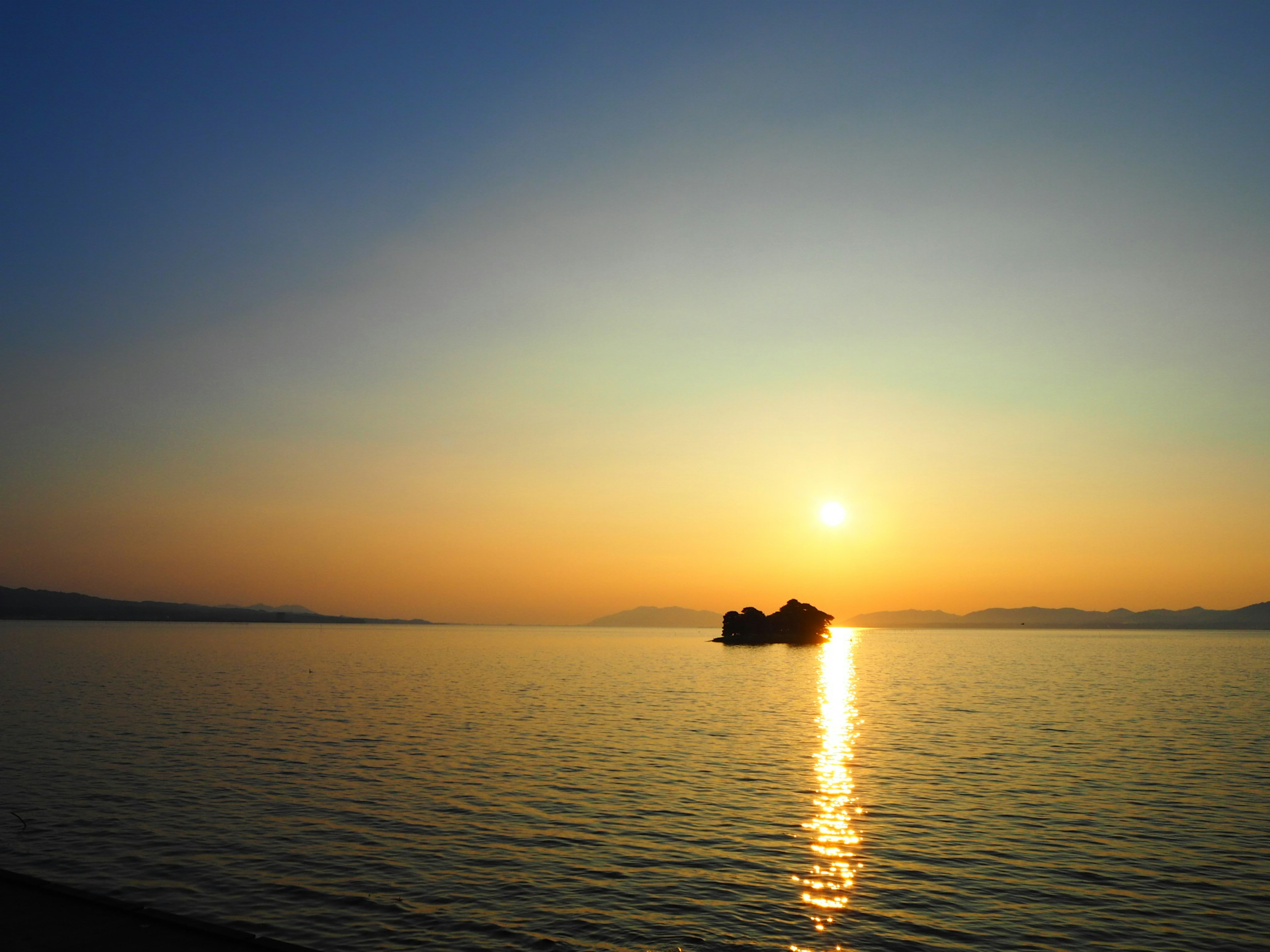 Sonnenuntergang über dem Wasser mit einer kleinen Insel im Silhouetten