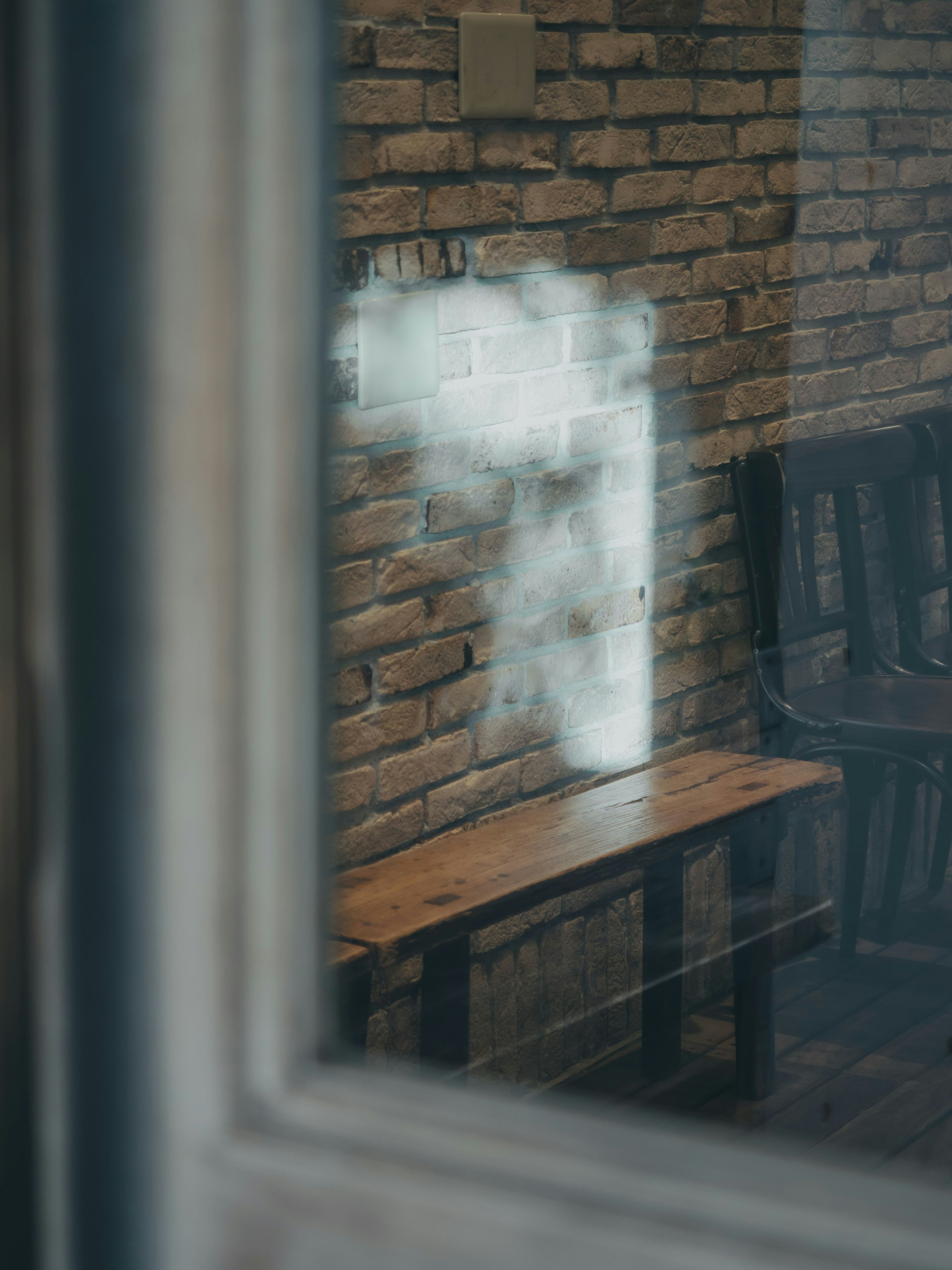 Image of a brick wall and wooden bench seen through a window with a smoky white cloud reflected on the wall