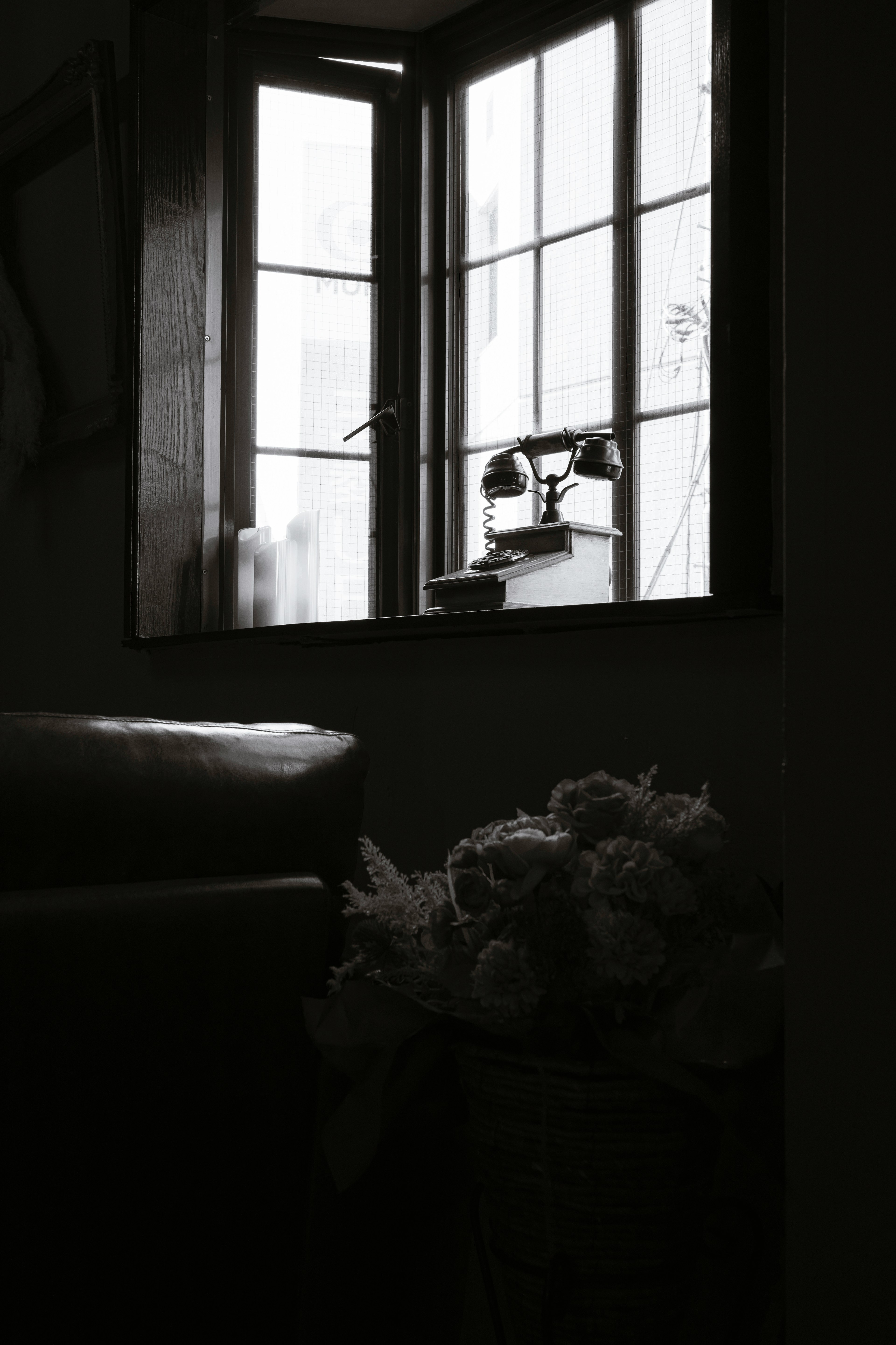 A corner of a room with light coming through the window a vase with flowers is visible