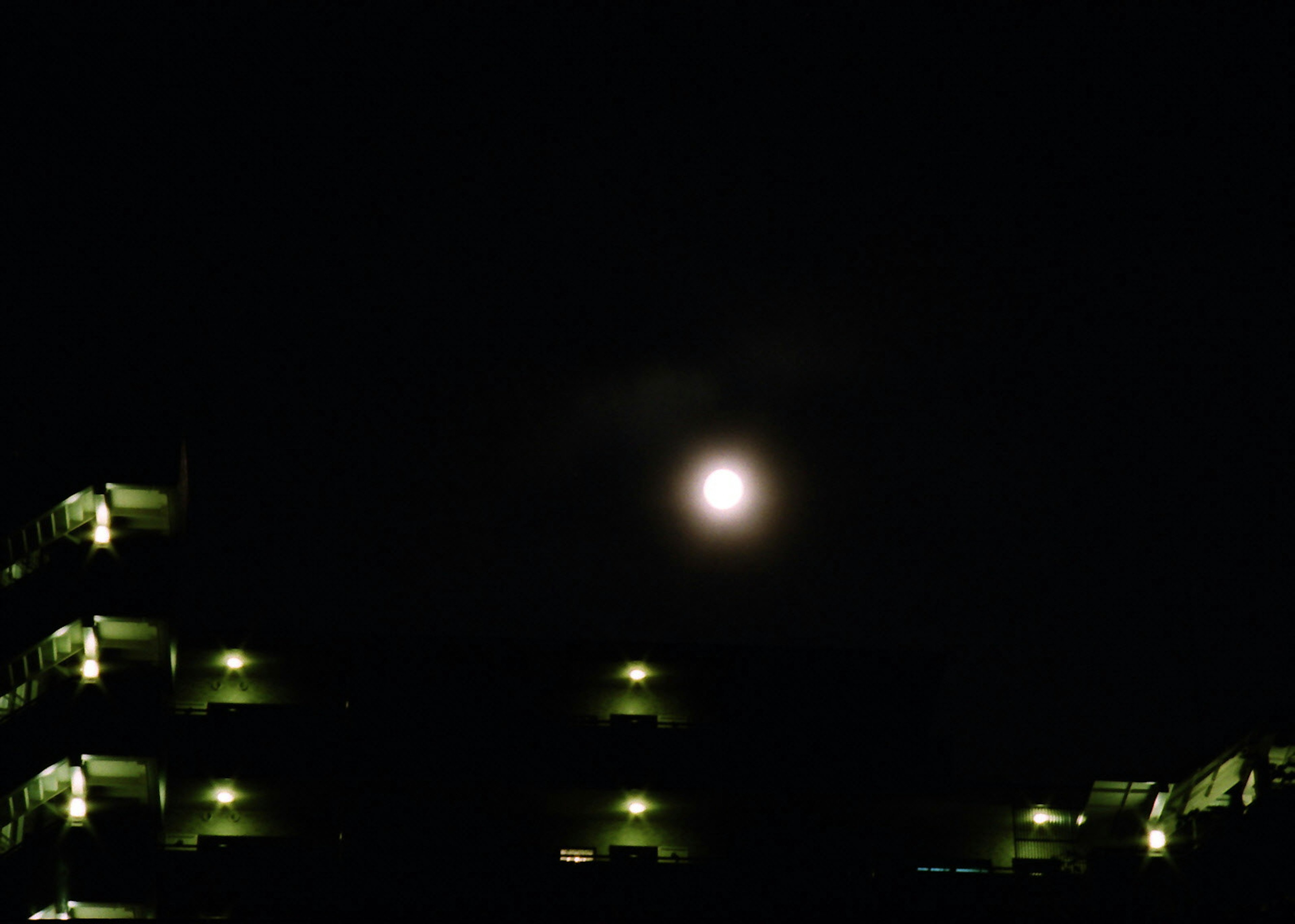 Bulan purnama cerah di langit malam dengan siluet bangunan gelap