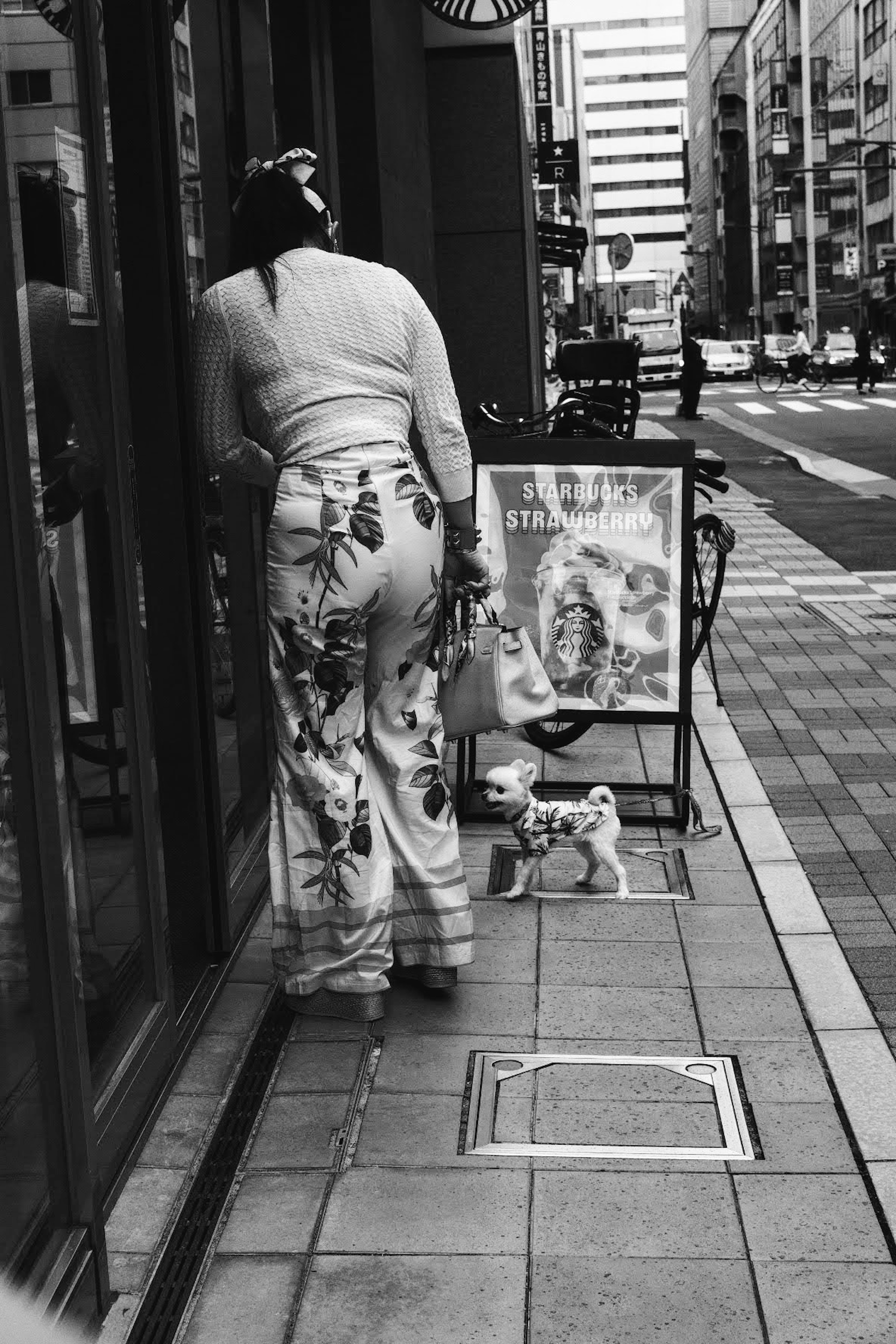 A woman standing in front of a store on the street in black and white featuring floral pants