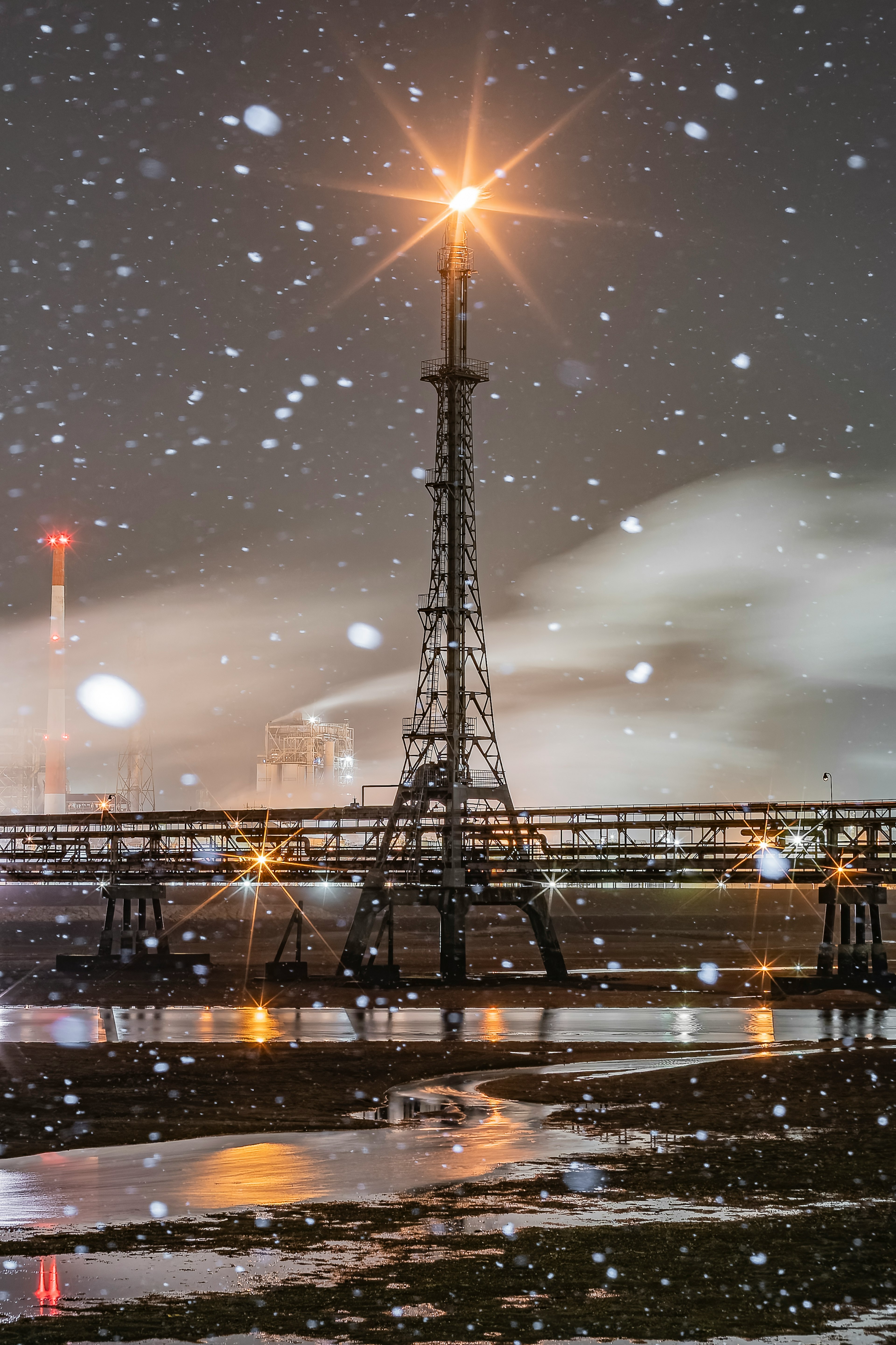 Radio tower illuminated in the snow at night with surrounding puddles