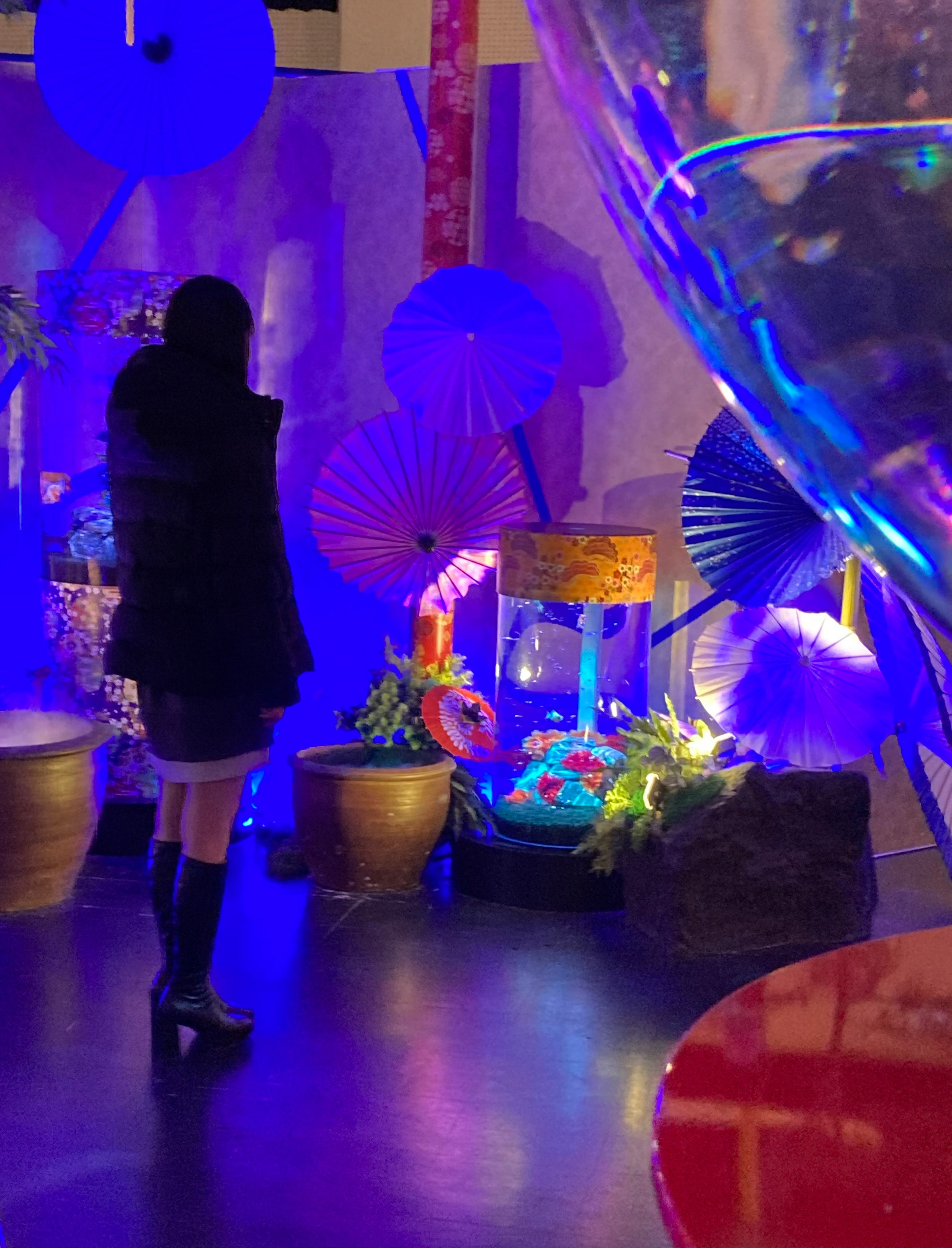 Mujer de pie frente a paraguas coloridos y un acuario decorativo iluminado por luces azules