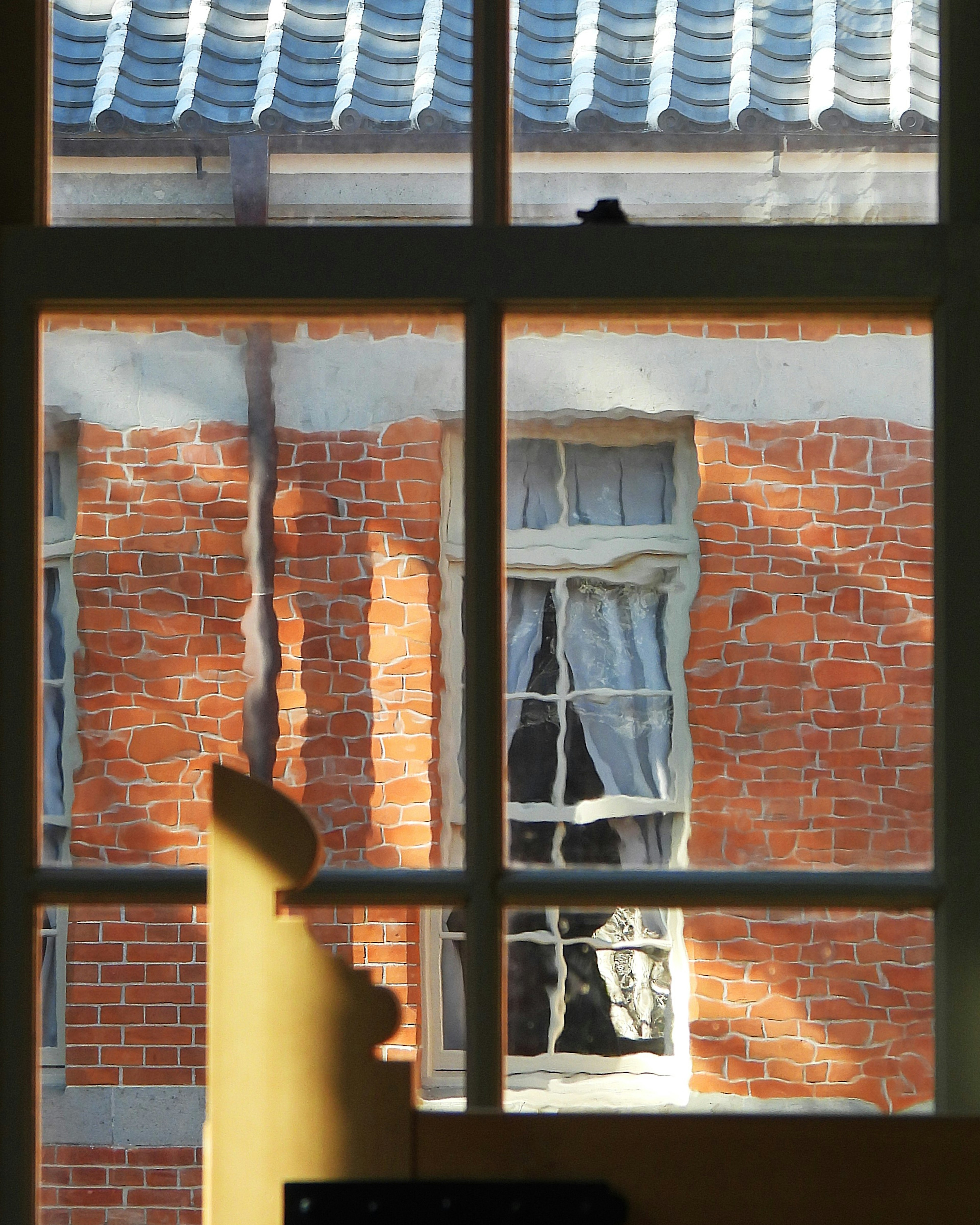 Blick durch ein Fenster auf eine Ziegelwand und Vorhänge eines alten Gebäudes