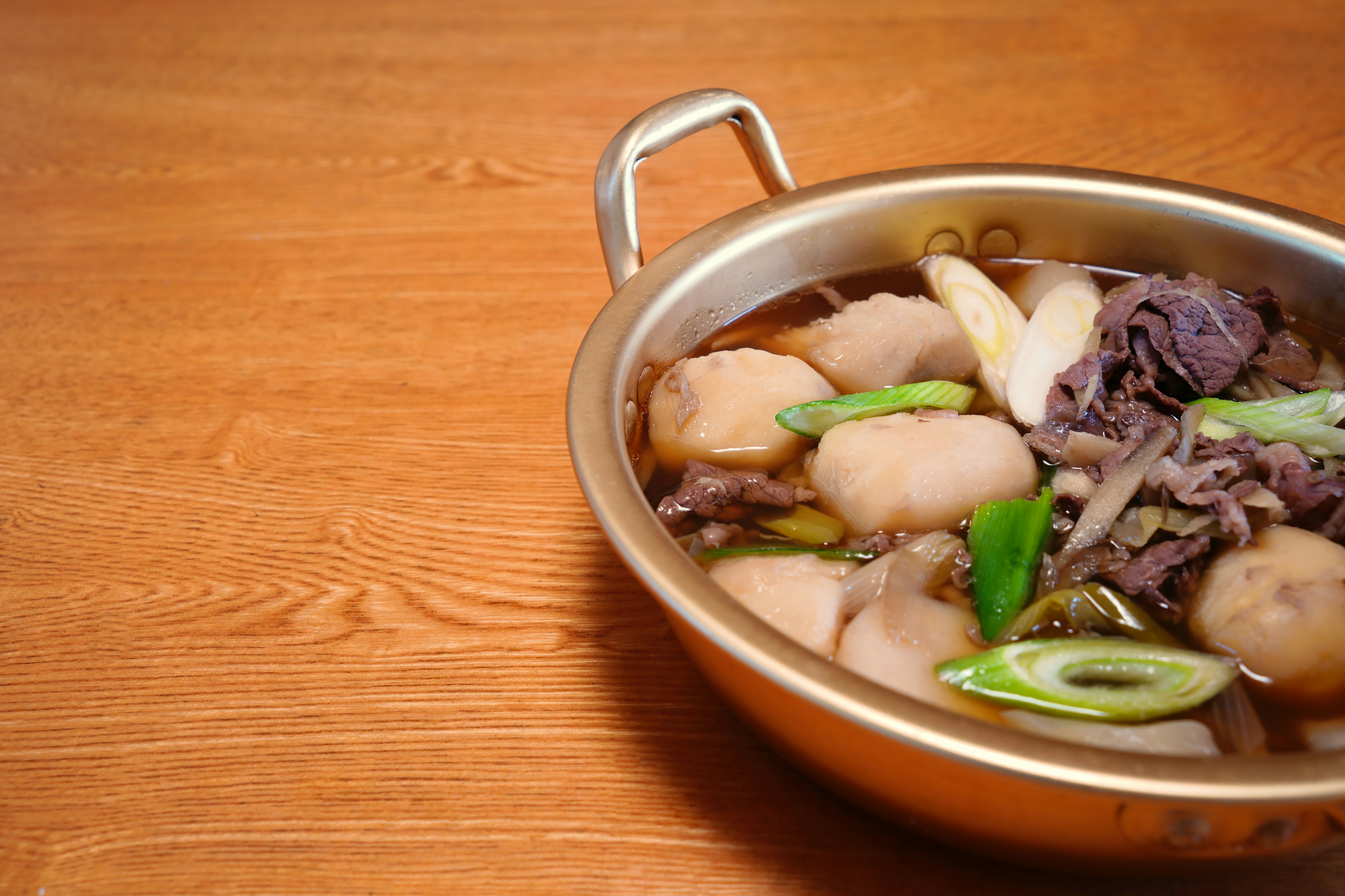 A pot of soup with meat and dumplings garnished with green onions