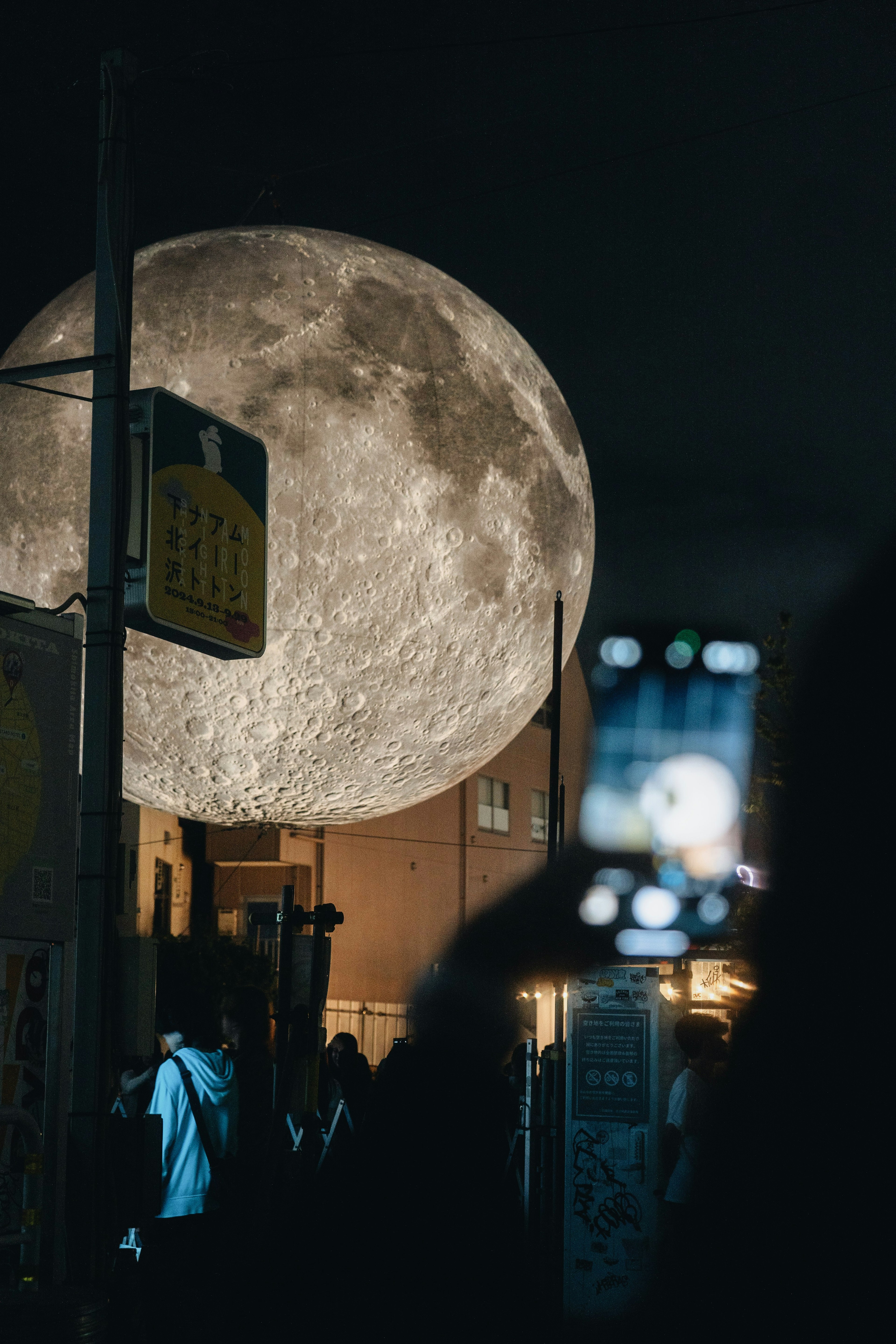 夜空に浮かぶ巨大な満月と人々が集まる風景