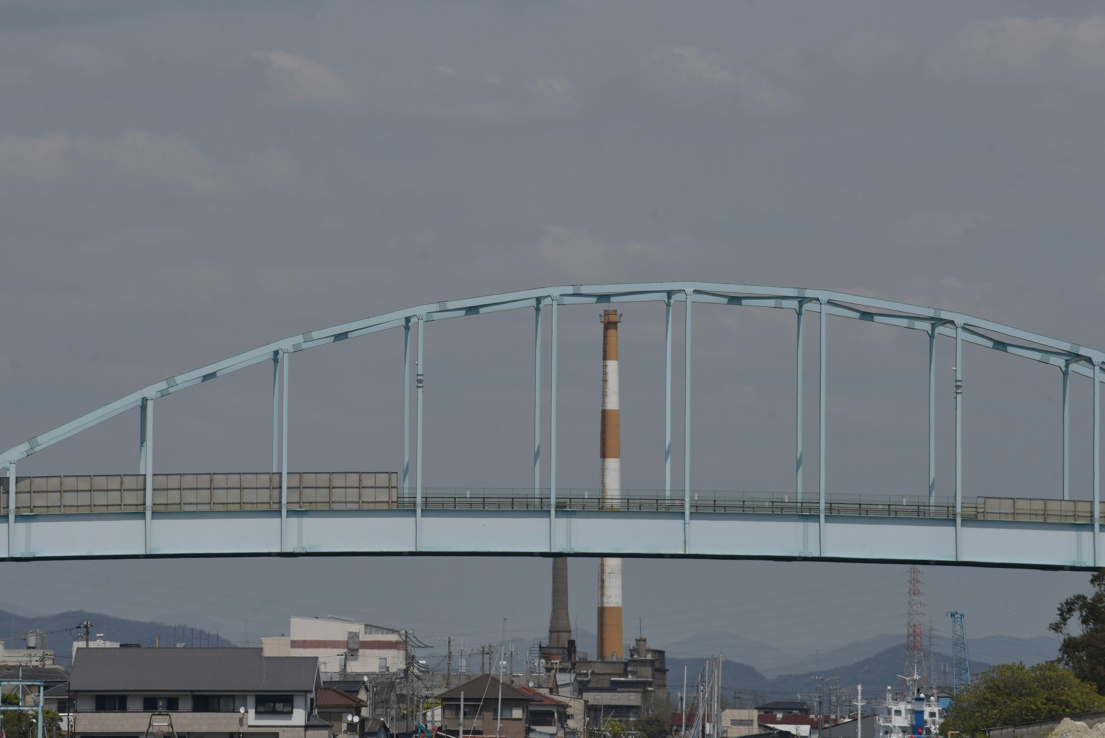 A blue arch bridge with a factory chimney in the background