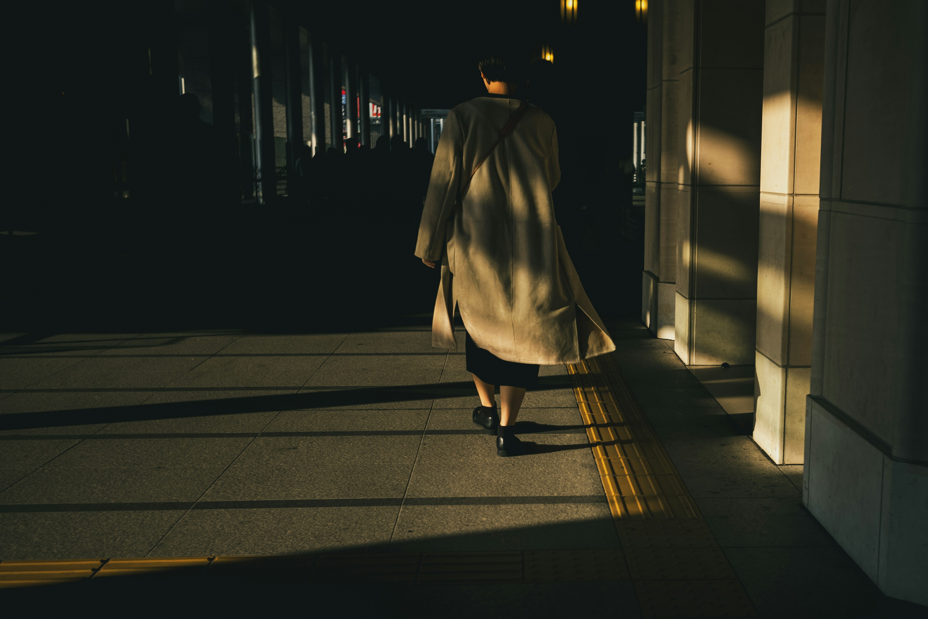 Femme marchant dans l'ombre portant un manteau clair et des chaussures