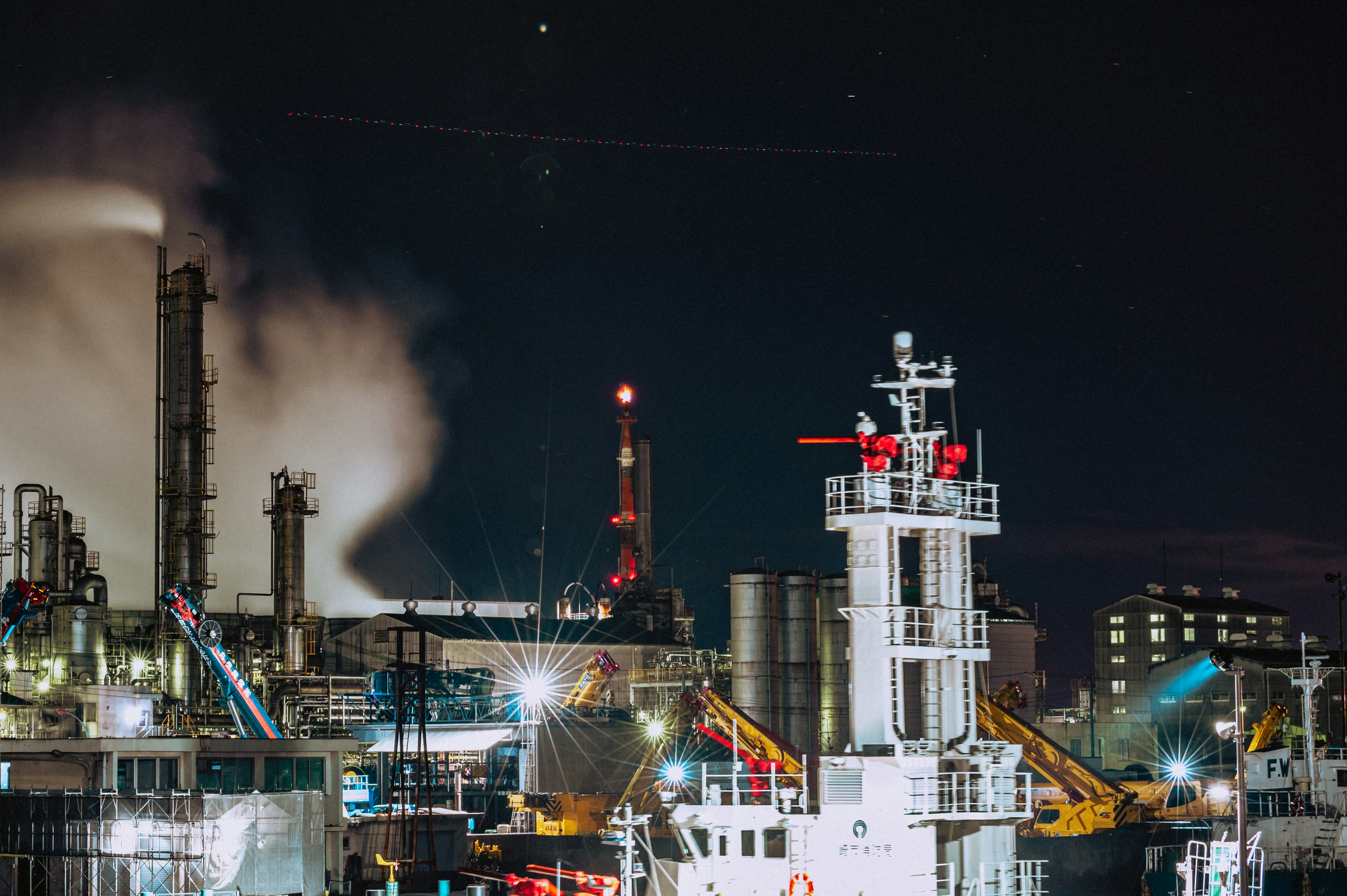 Escena de puerto industrial nocturno con un barco y humo