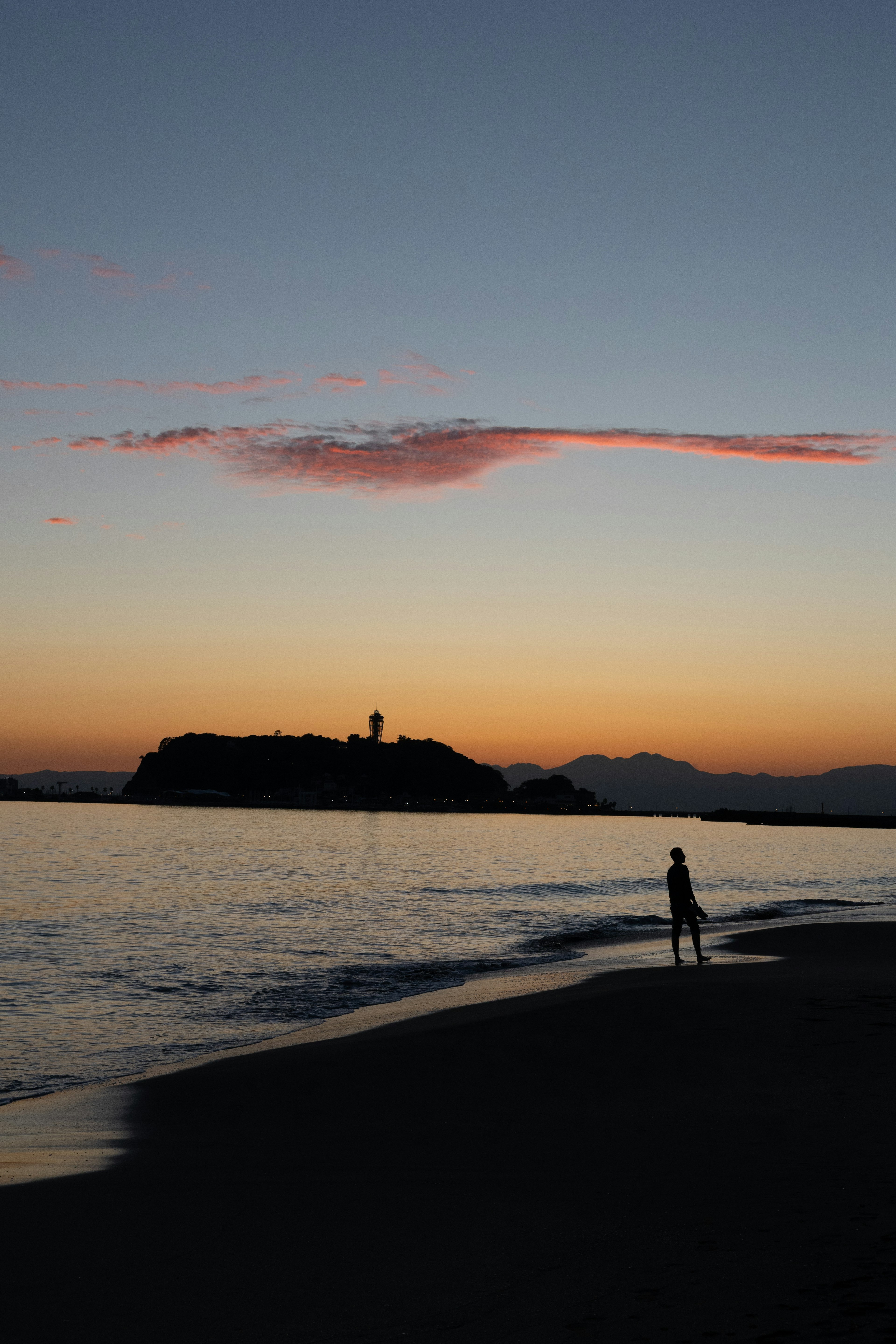 Silhouette di una persona su una spiaggia al tramonto con un'isola sullo sfondo