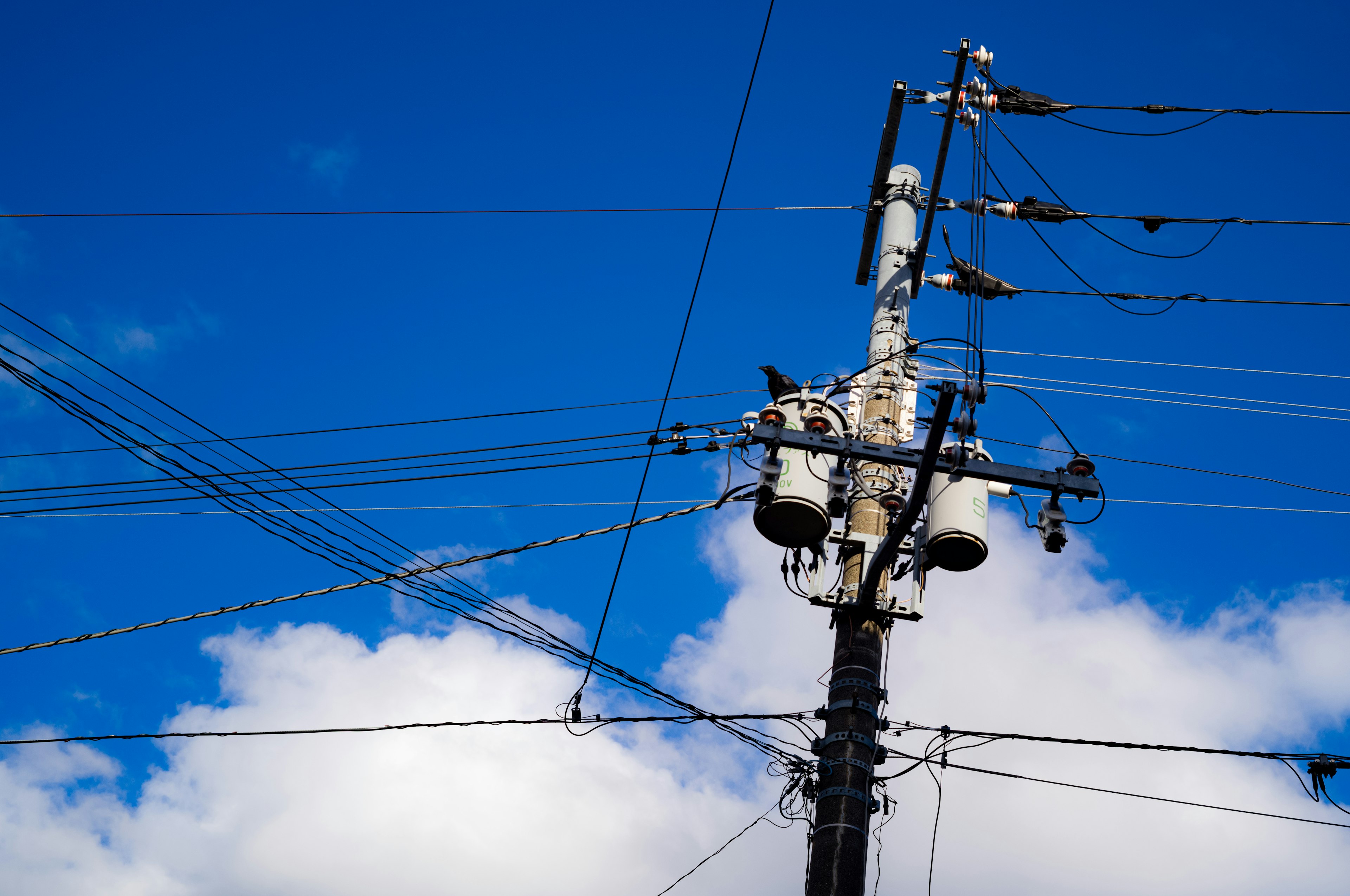 Poste de electricidad con cables contra un cielo azul y nubes blancas