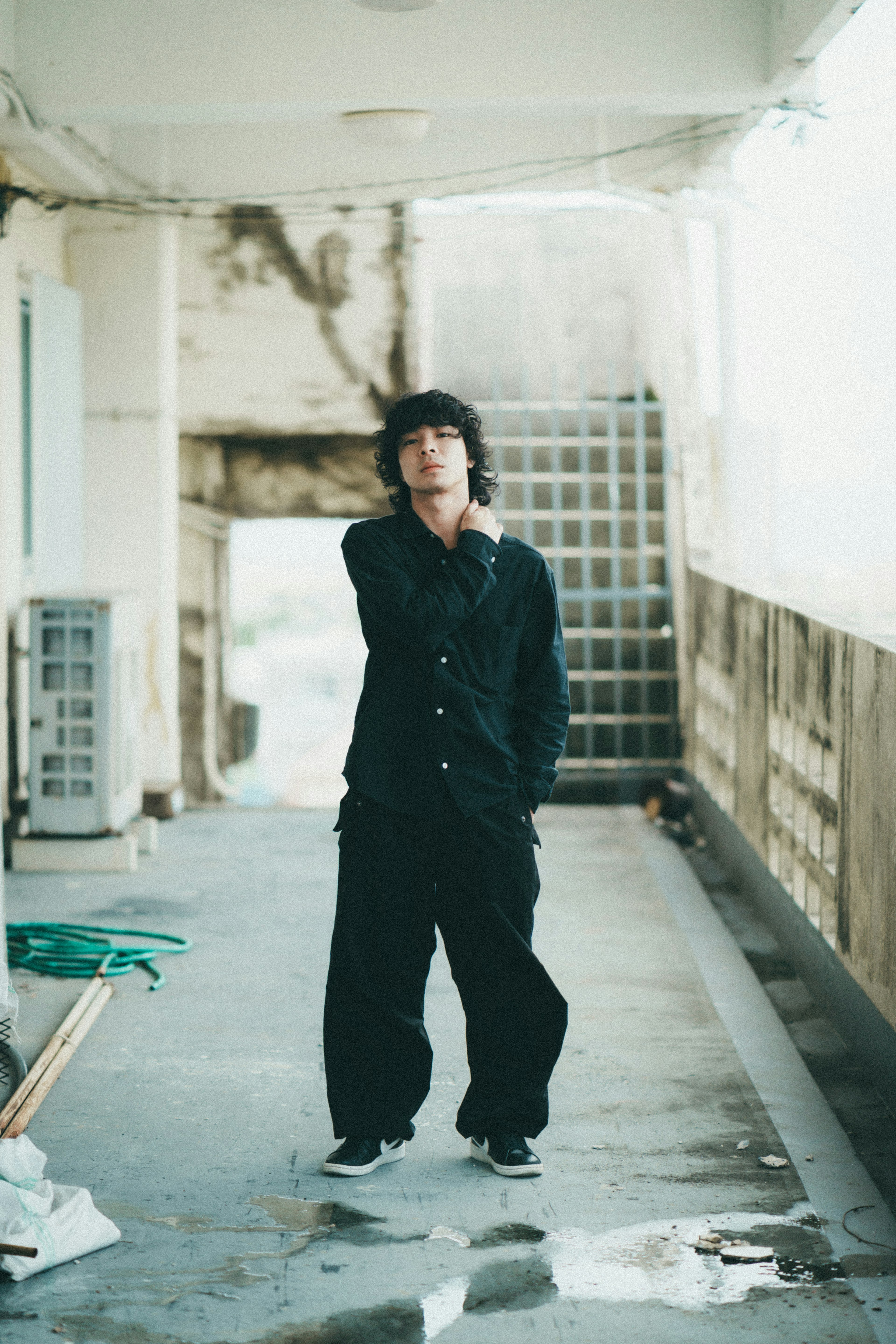 A man in black clothing standing in a hallway with an old building wall in the background