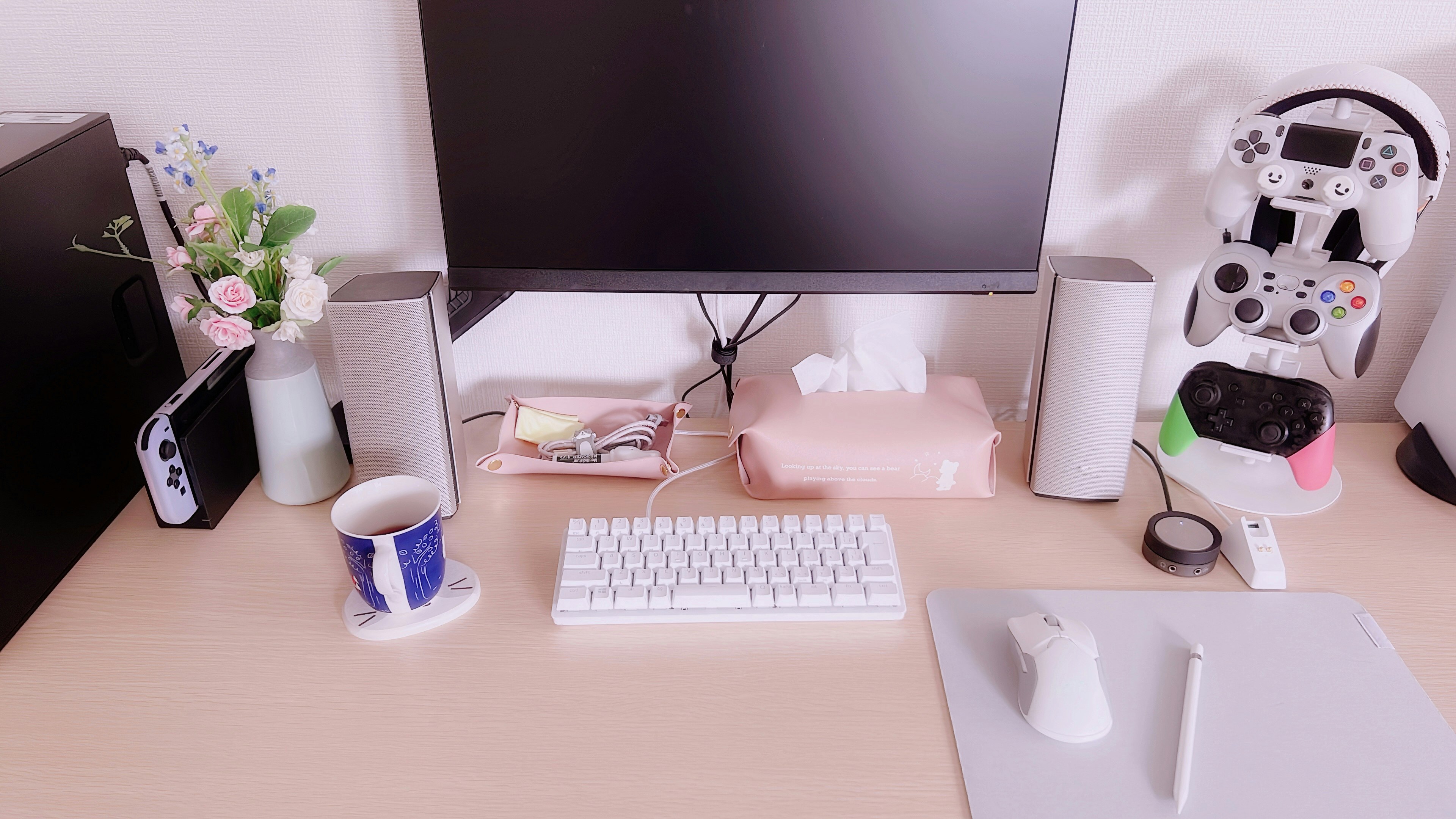 Schreibtisch mit Monitor und weißer Tastatur sowie einer Tasse und einer Vase