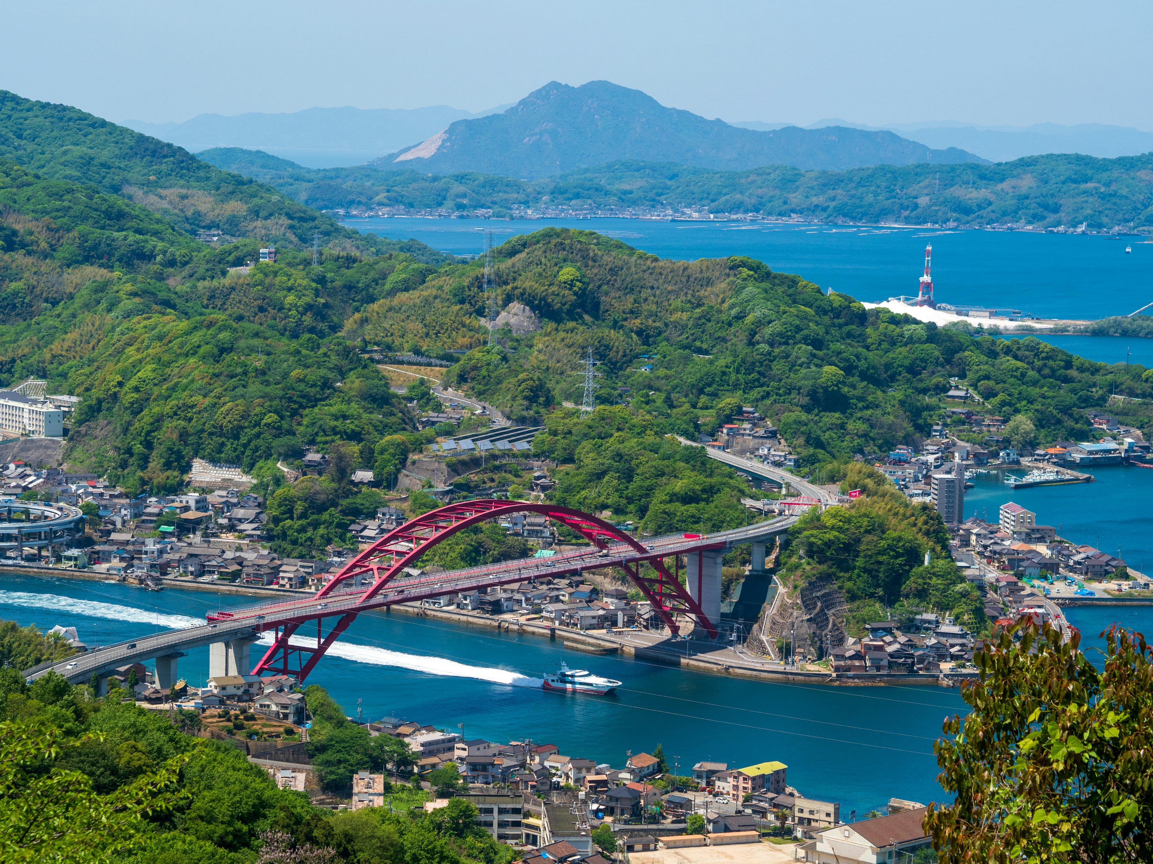 Vue pittoresque d'un pont en arc rouge entouré de la mer bleue et des montagnes vertes