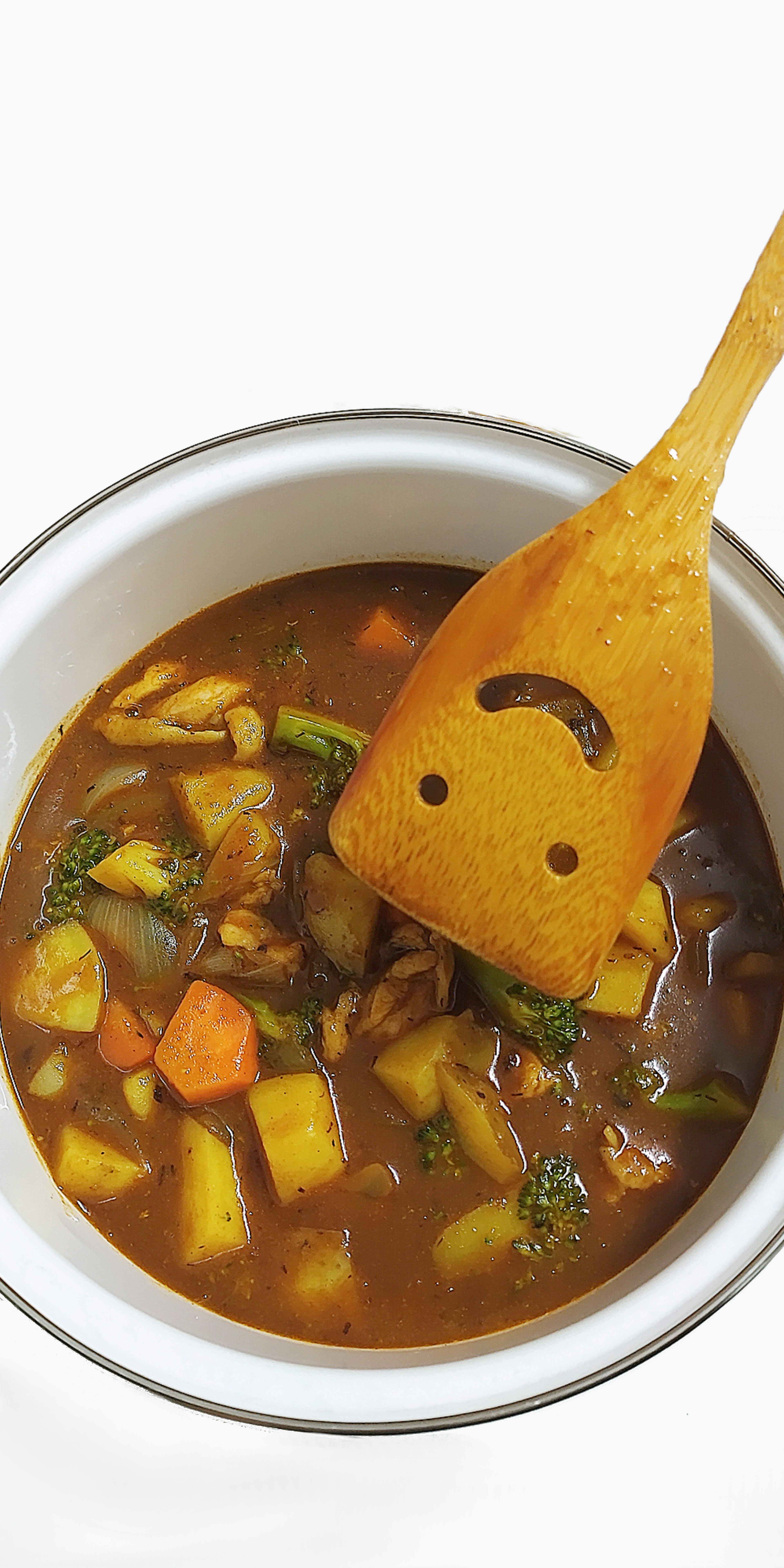 Olla de curry de verduras con una cuchara de madera sonriente