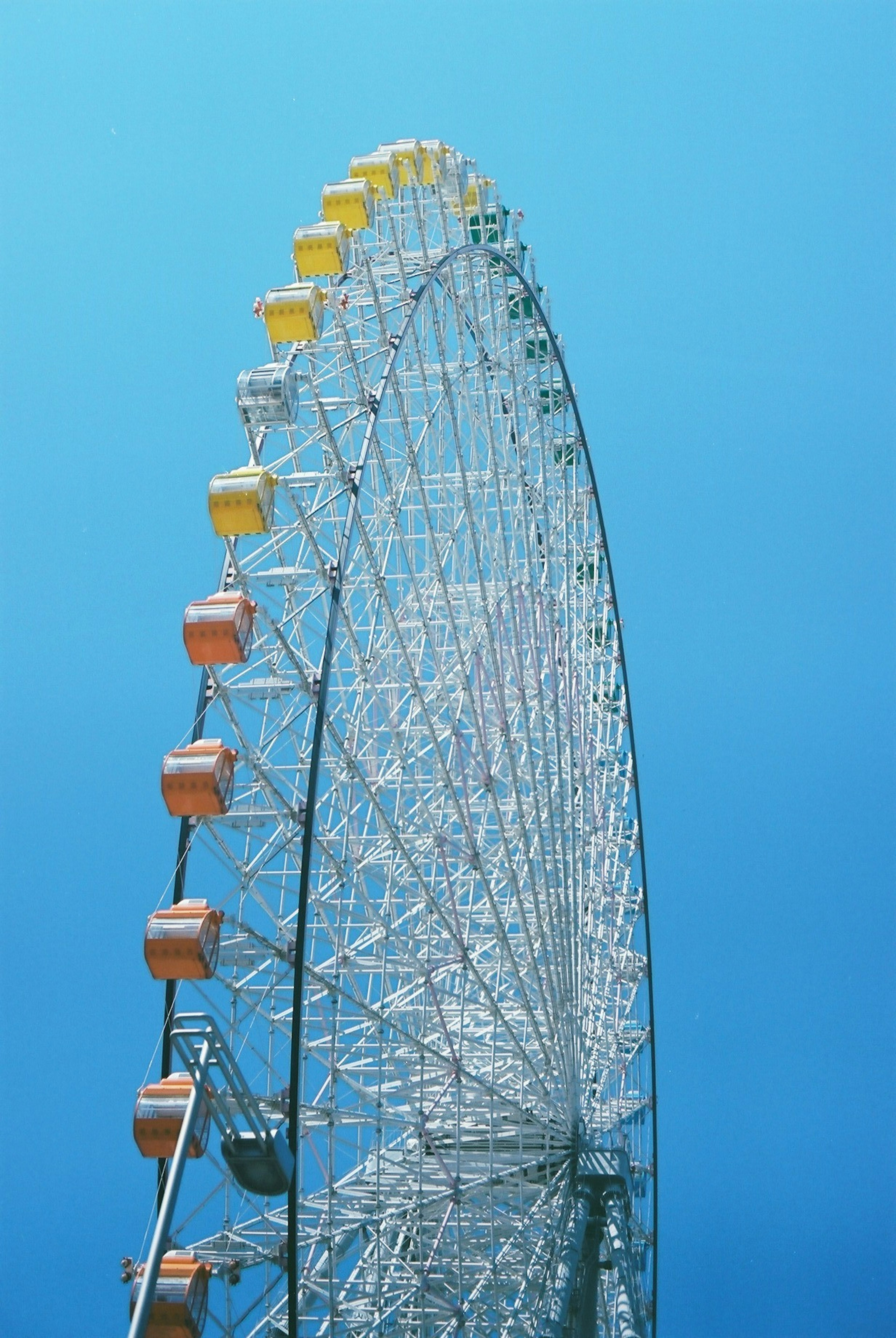 Vue latérale d'une grande roue colorée sous un ciel bleu avec diverses capsules