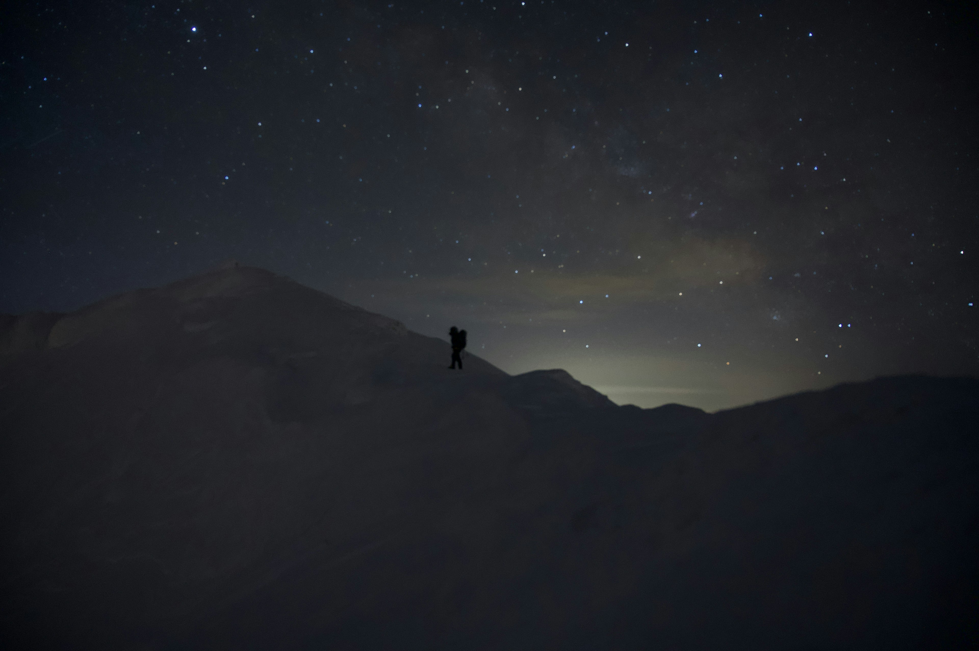 星空の下に立つ登山者と雪に覆われた山々