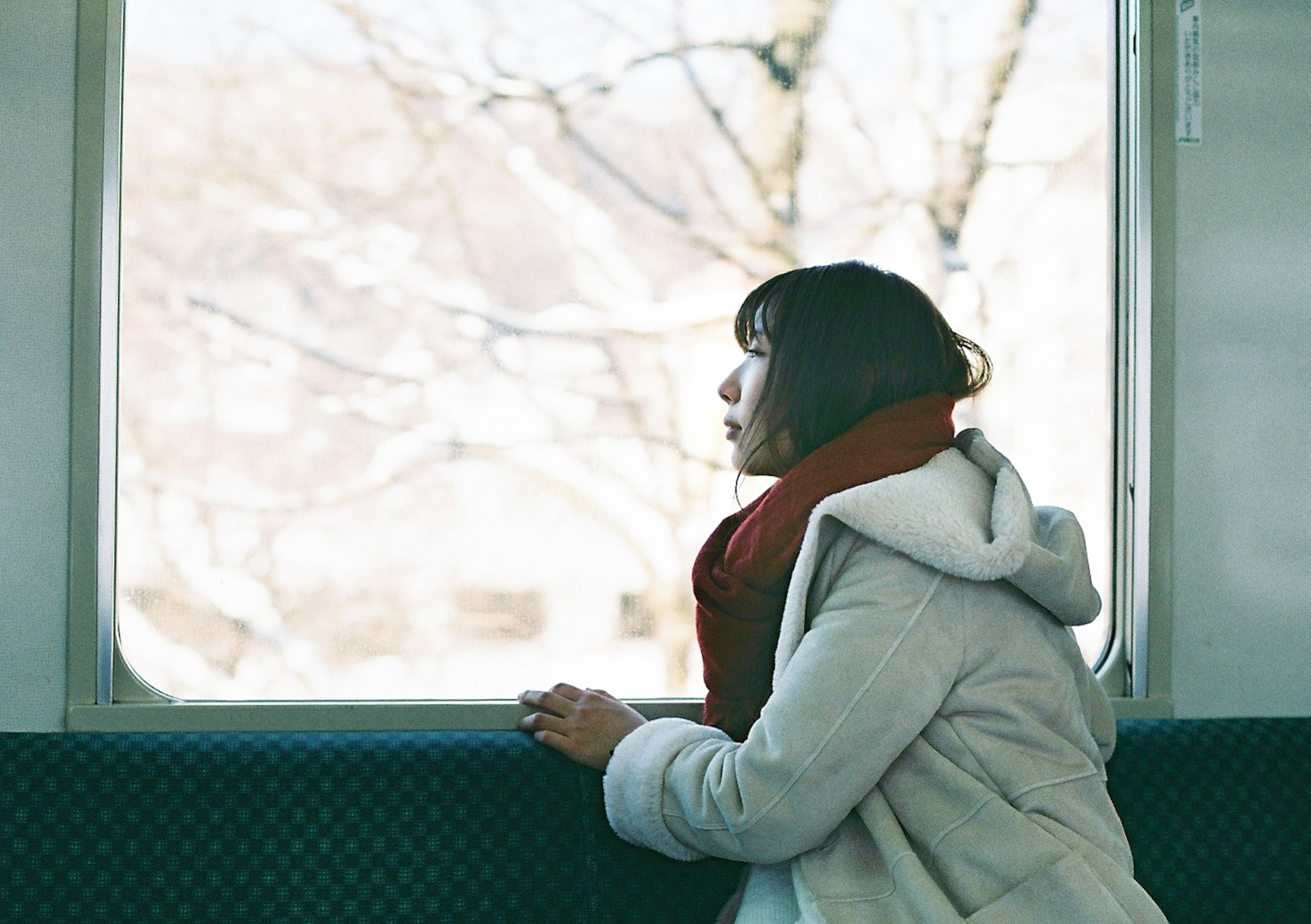 Woman gazing out of a train window wearing a white coat and red scarf