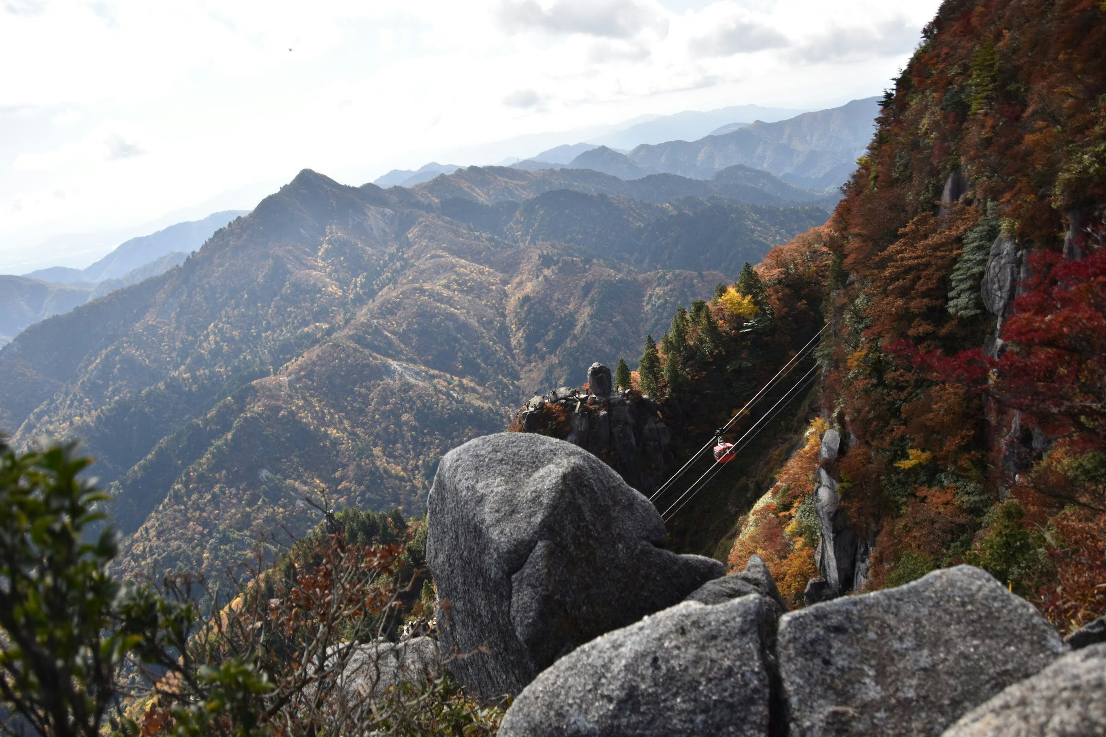 秋の紅葉が広がる山岳風景と岩の近くに立つ人