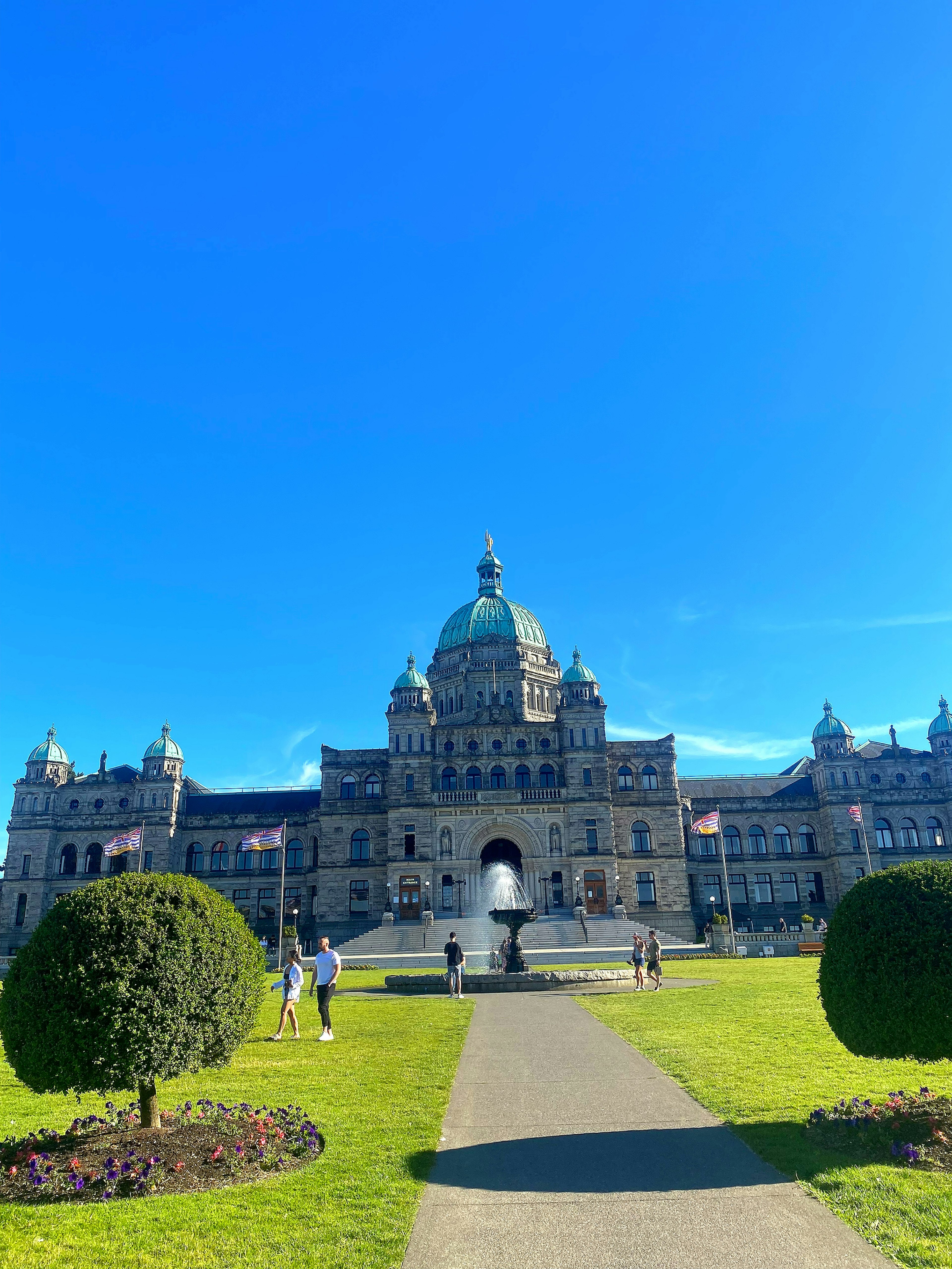 Grand exterior of the British Columbia Legislature under a clear blue sky with manicured gardens