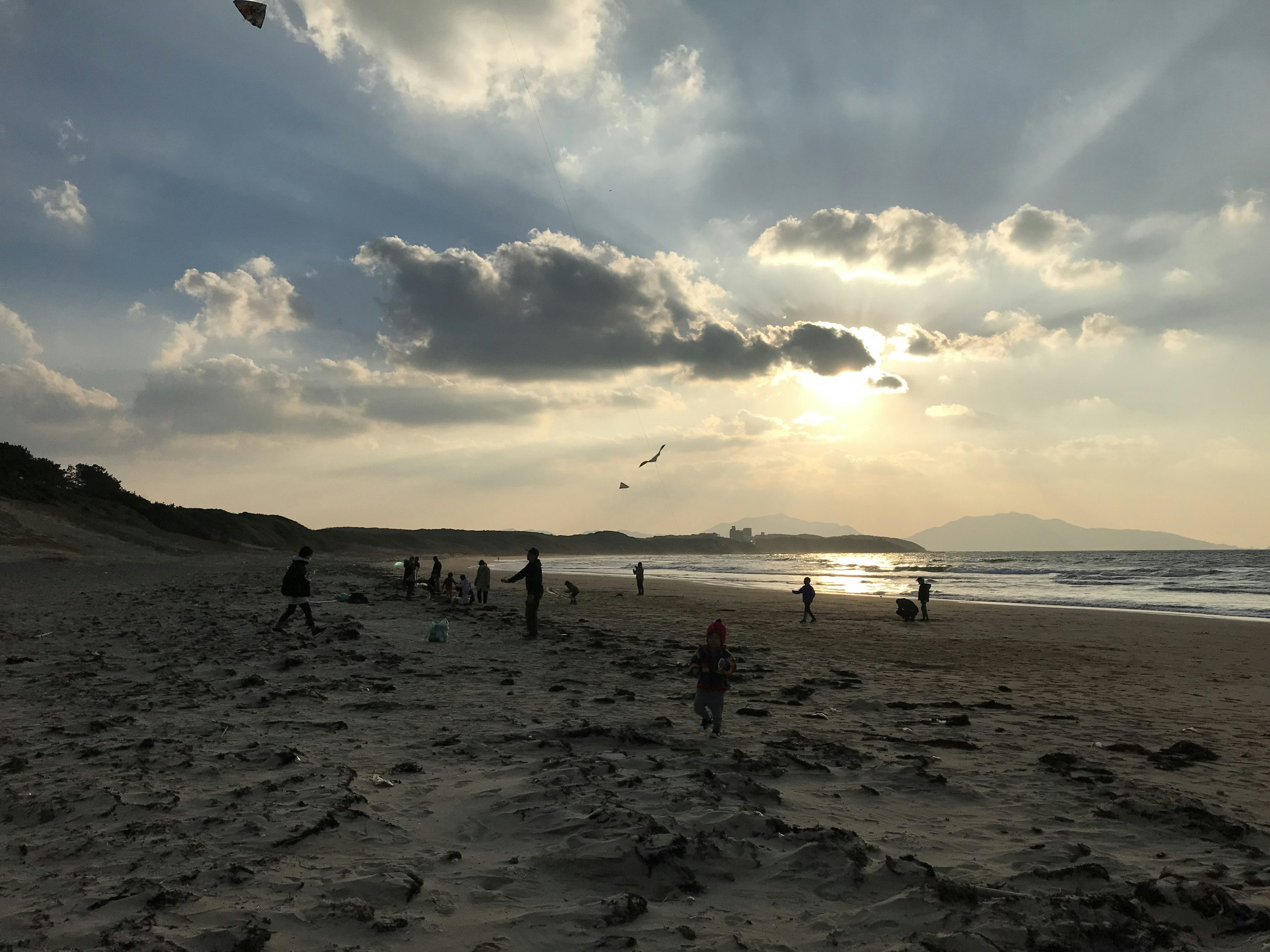 夕日が沈むビーチで遊ぶ人々と風に揺れる凧