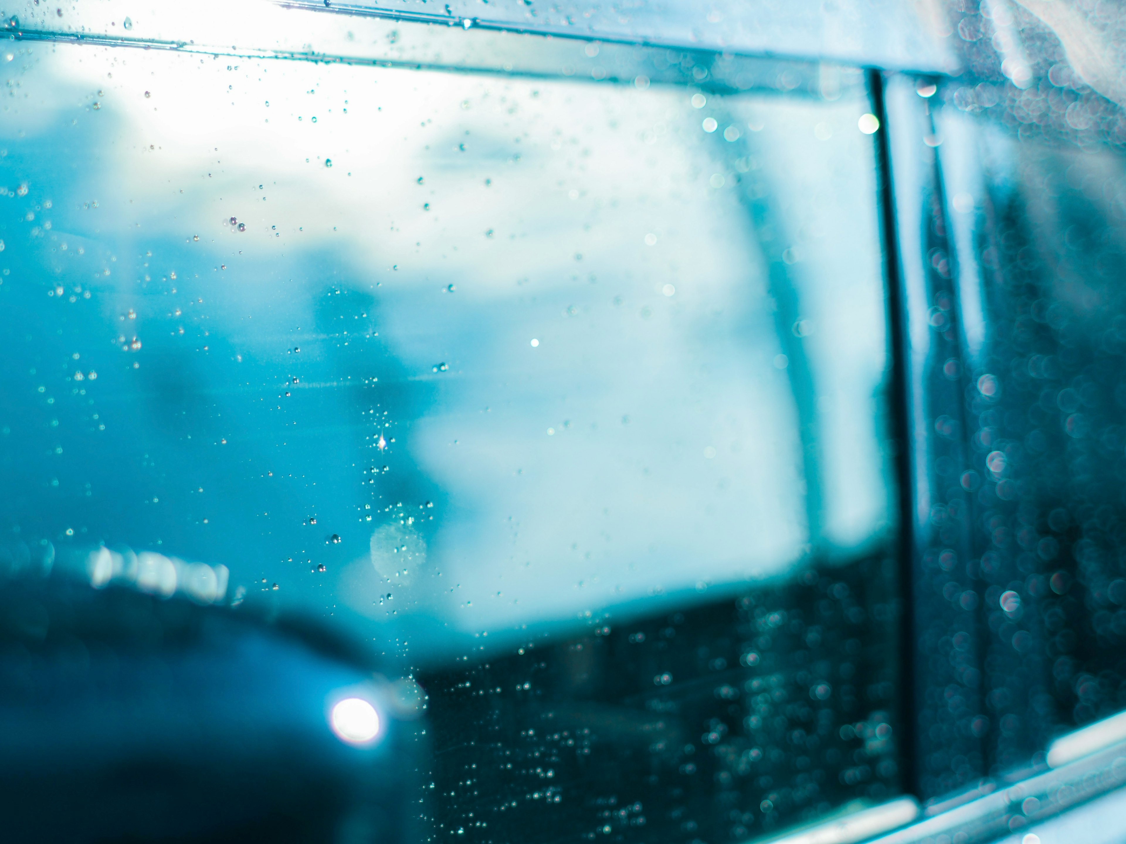 Gros plan sur une vitre de voiture avec des gouttes d'eau arrière-plan flou dans des tons bleus