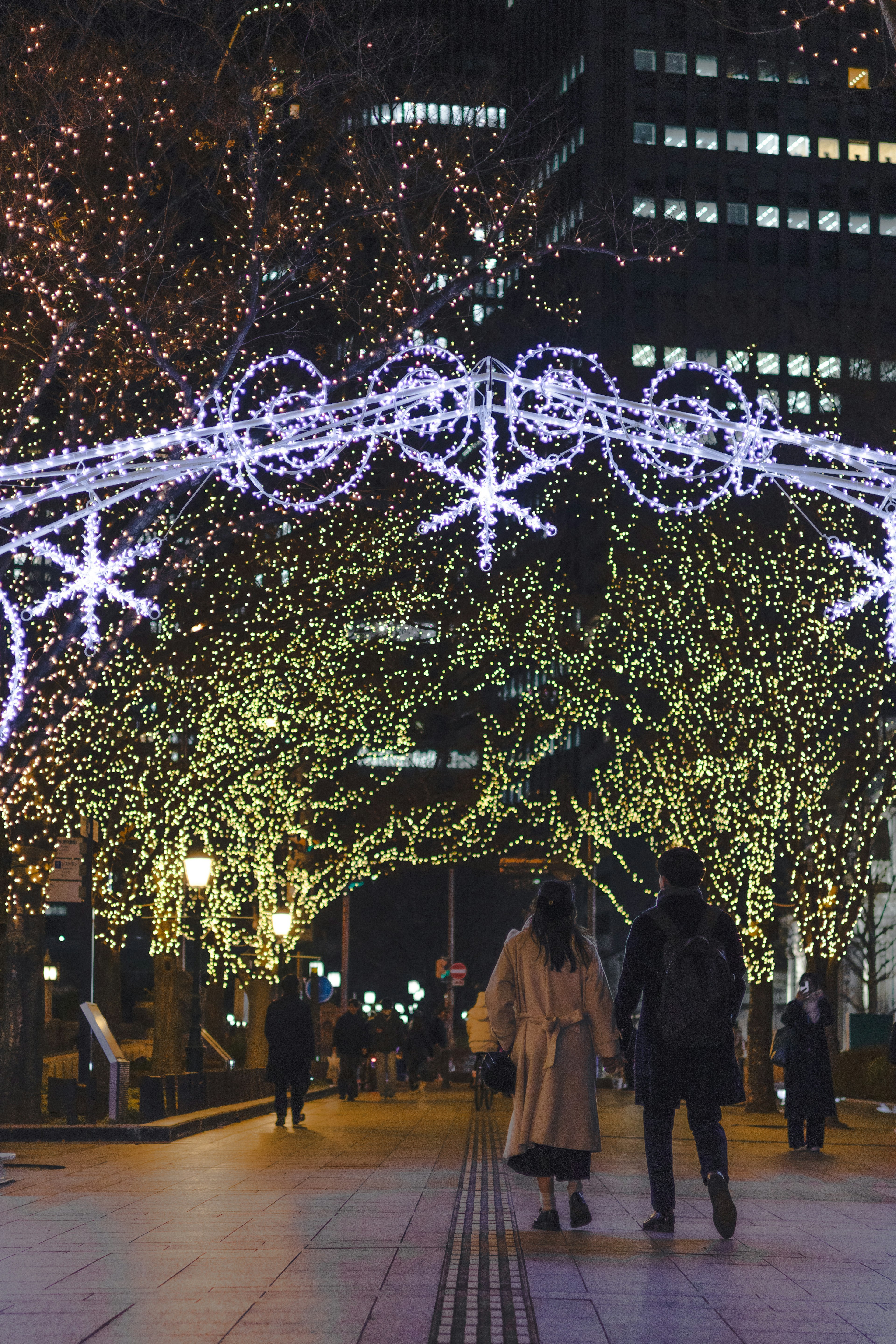 夜の街で光るクリスマスイルミネーションのアーチを歩く人々